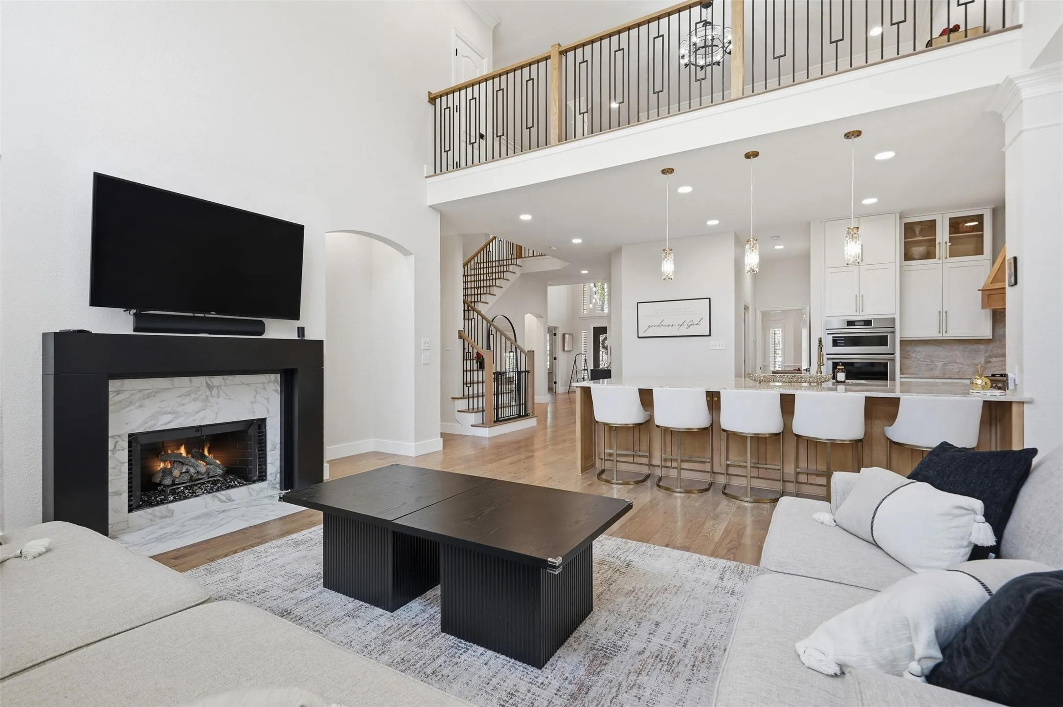 Expansive living area with high ceilings, a fireplace featuring a black mantel and light-toned surround, and light wood-finish flooring