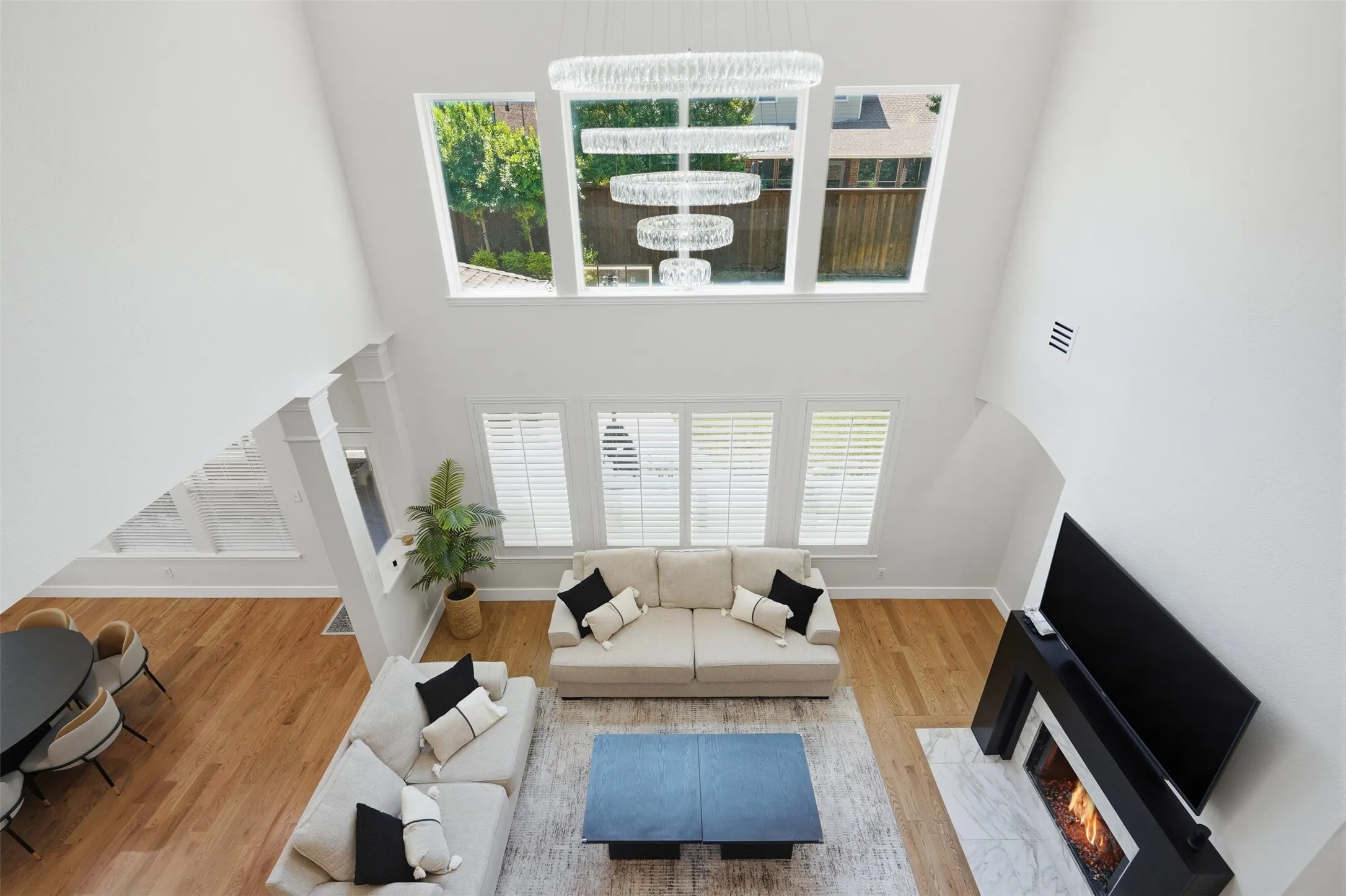 Vaulted ceiling with a tiered chandelier, multiple transom windows, wood-finish flooring, and a fireplace with a stone surround