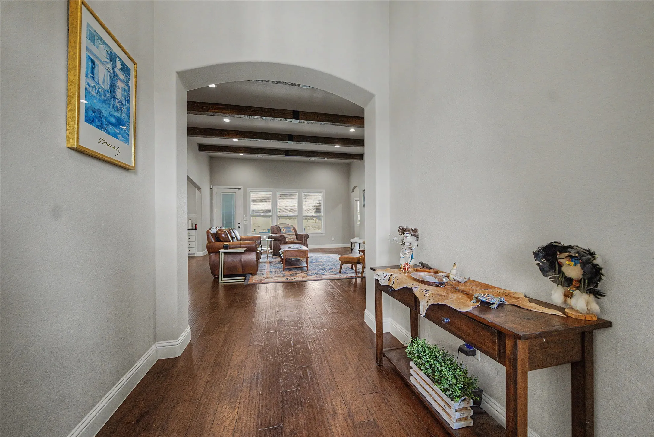 Arched entryway leading to a living space with wood-finish flooring, exposed ceiling beams, recessed lighting, and multiple windows
