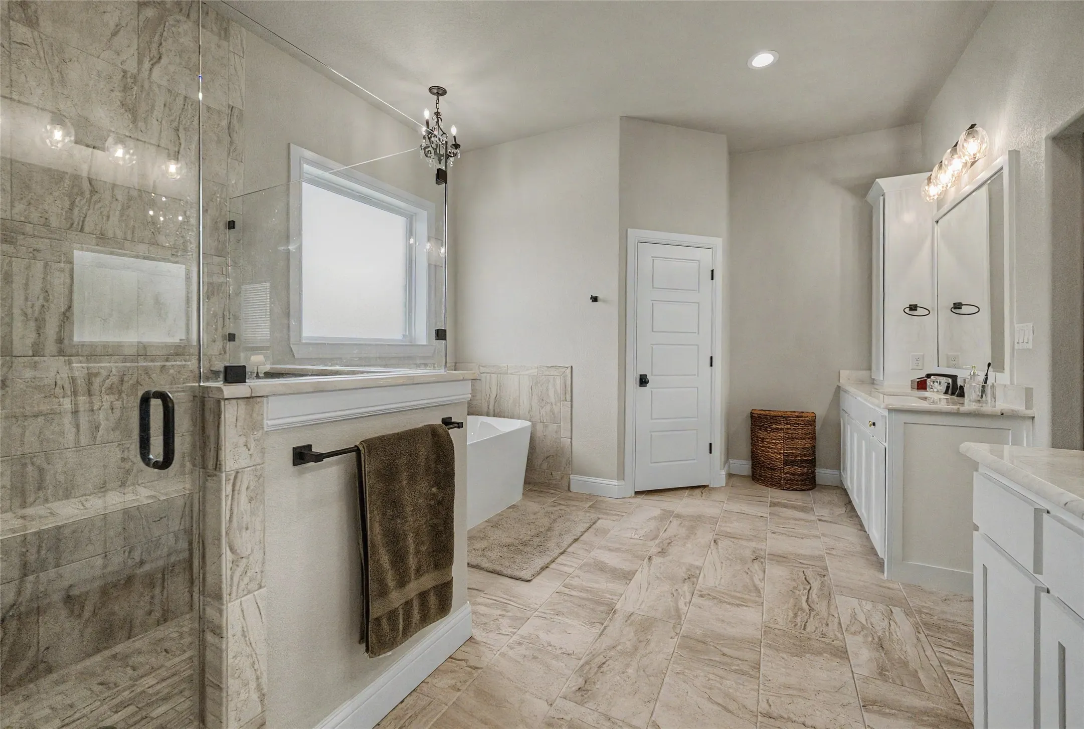 Spacious bathroom featuring large format tile flooring, a glass-enclosed shower with integrated niche, and a freestanding soaking tub