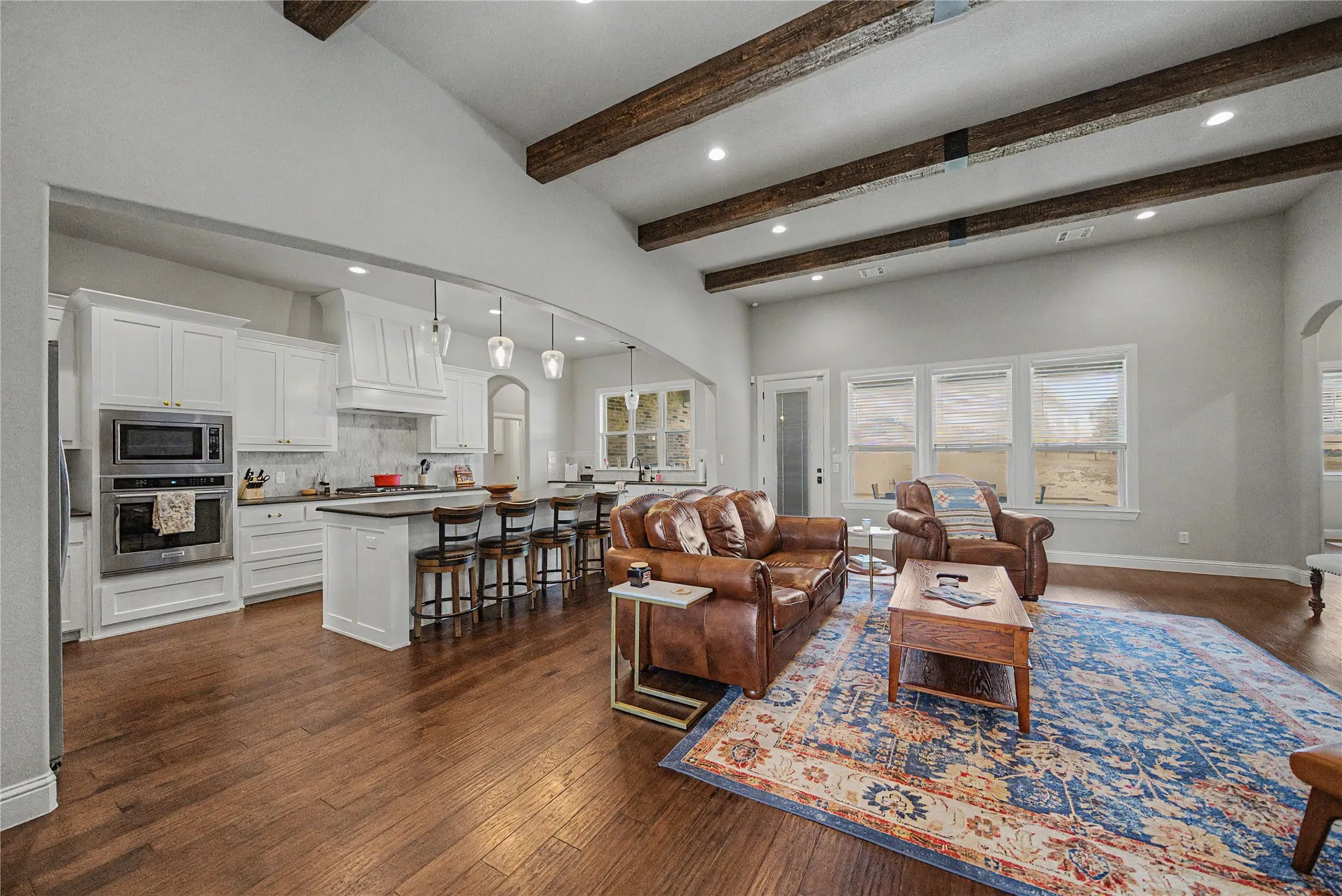 Open-concept living area with high vaulted ceilings featuring exposed wood beams and recessed lighting