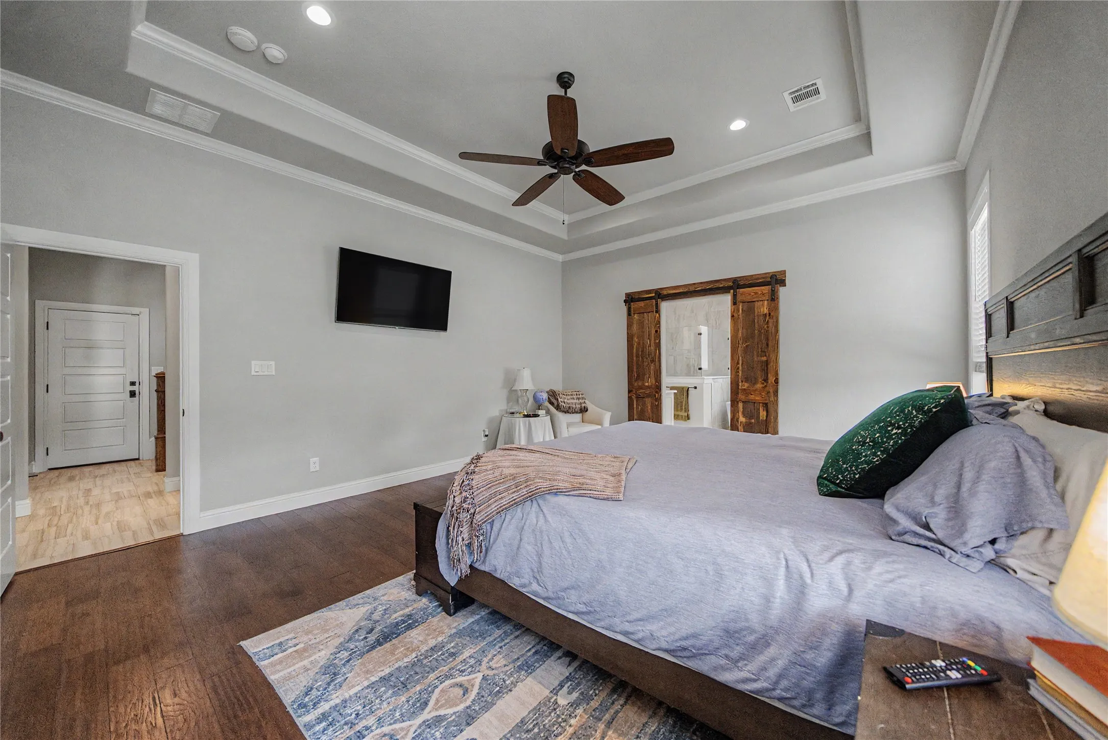 Spacious bedroom featuring wood-finish flooring and a tray ceiling with a ceiling fan