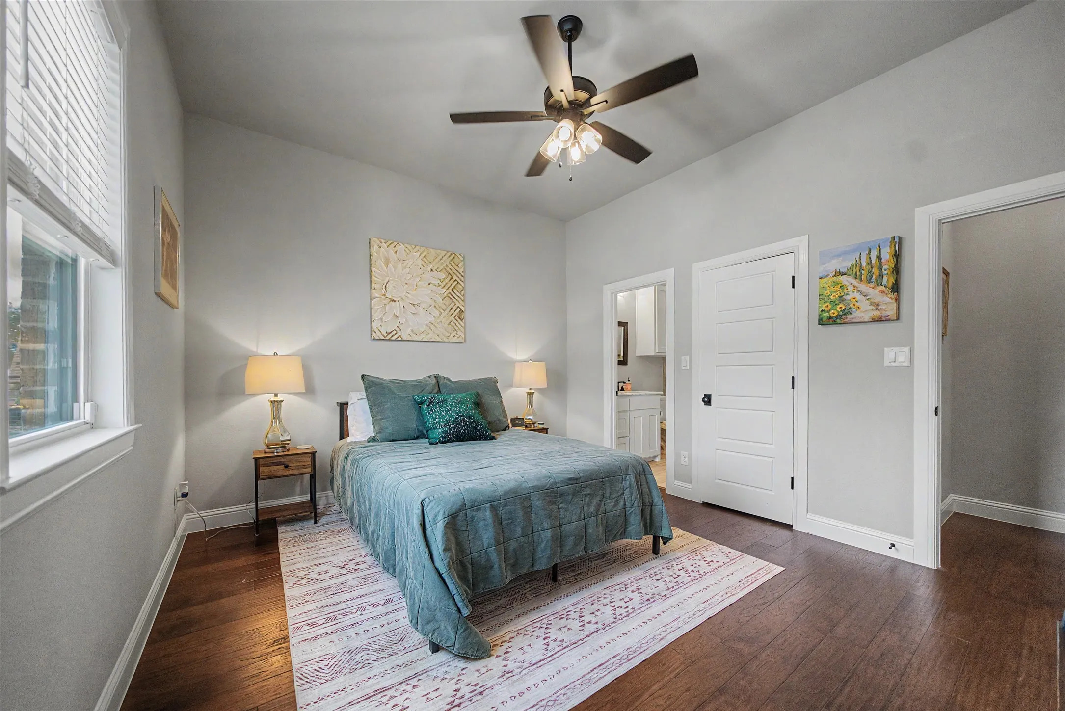 Vaulted ceiling bedroom featuring wood-finish flooring, a ceiling fan with light, a window with blinds, and white paneled doors