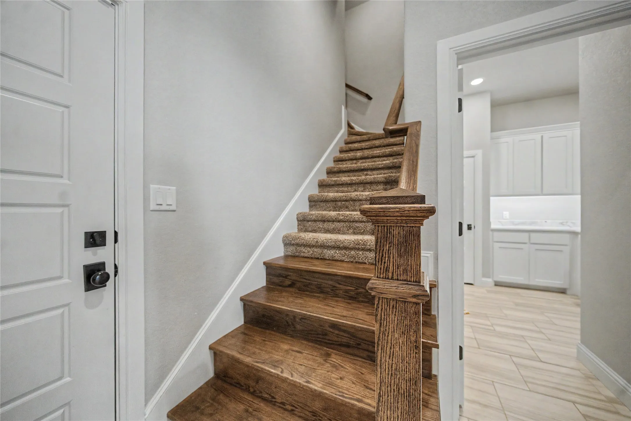 Wood-finish staircase featuring carpeted treads and a carved newel post