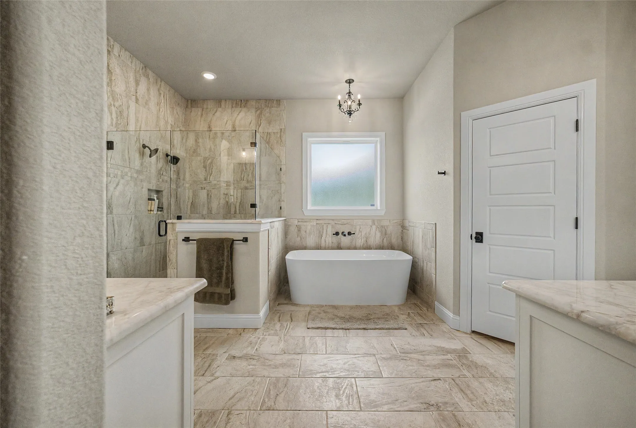 Spacious bathroom featuring a frameless glass shower enclosure, a freestanding soaking tub, and a decorative chandelier