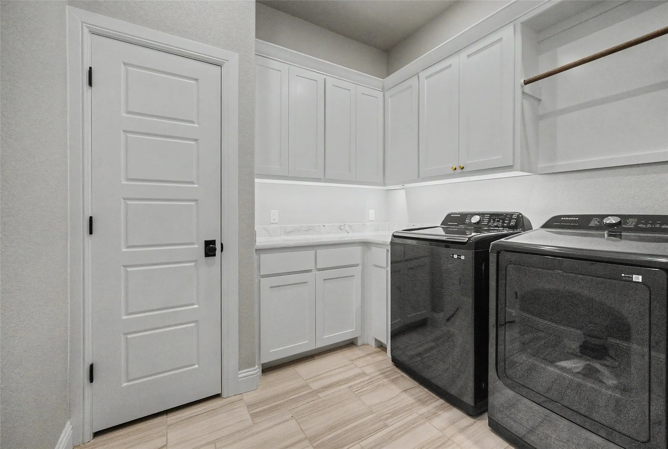 Laundry room featuring extensive white cabinetry, light-toned countertop, wood-finish flooring, and a built-in hanging rod