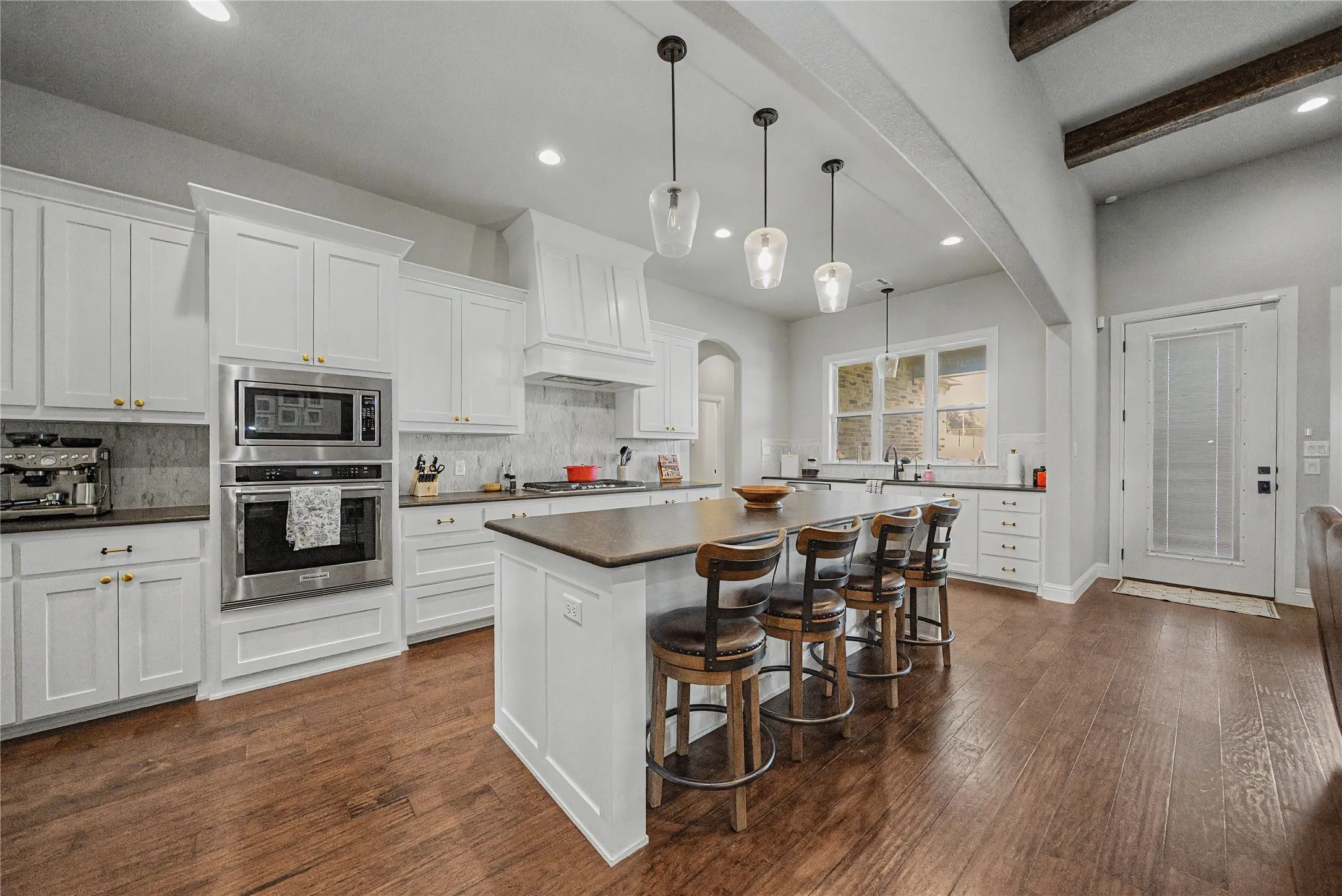 Spacious kitchen featuring an expansive center island with seating, stainless steel double oven, white cabinetry, dark countertops, and wood-finish flooring