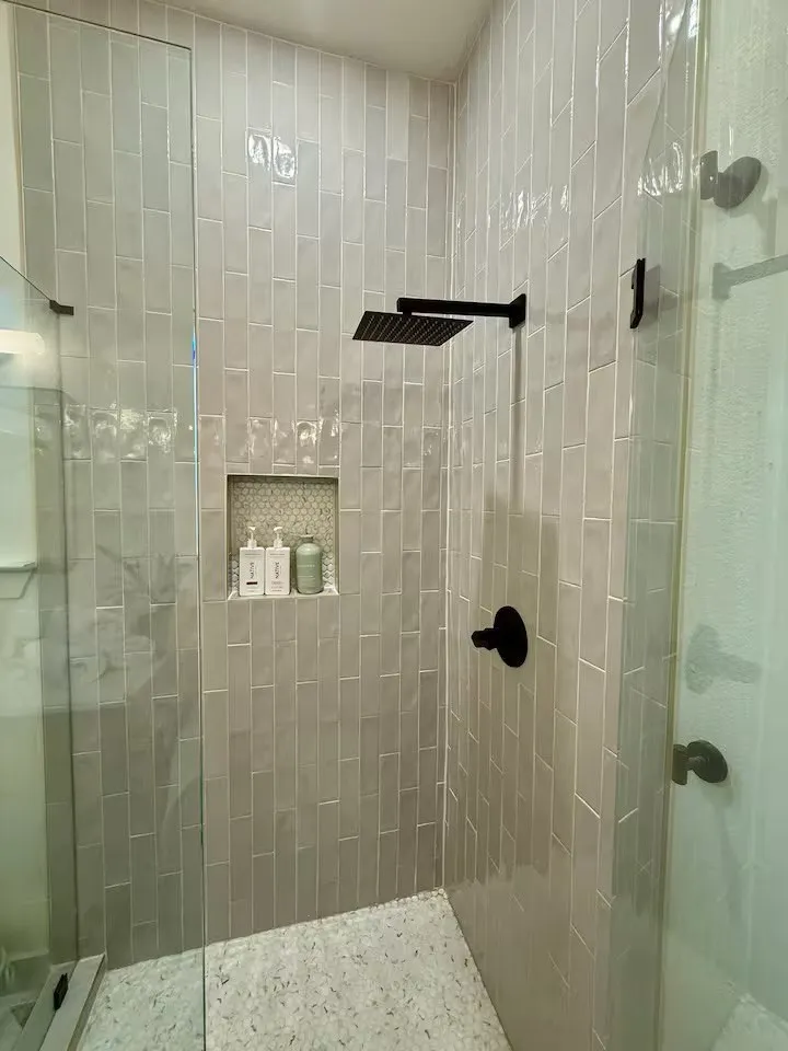 Modern shower enclosure featuring clear glass panels, vertical subway tile, a built-in niche with mosaic tile, a matte black rainfall showerhead, and coordinating matte black fixtures