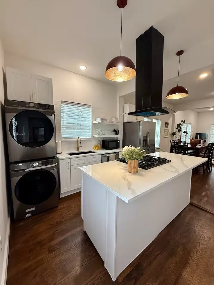 Contemporary kitchen featuring a white island with a cooktop, stone-finish countertop, and pendant lighting