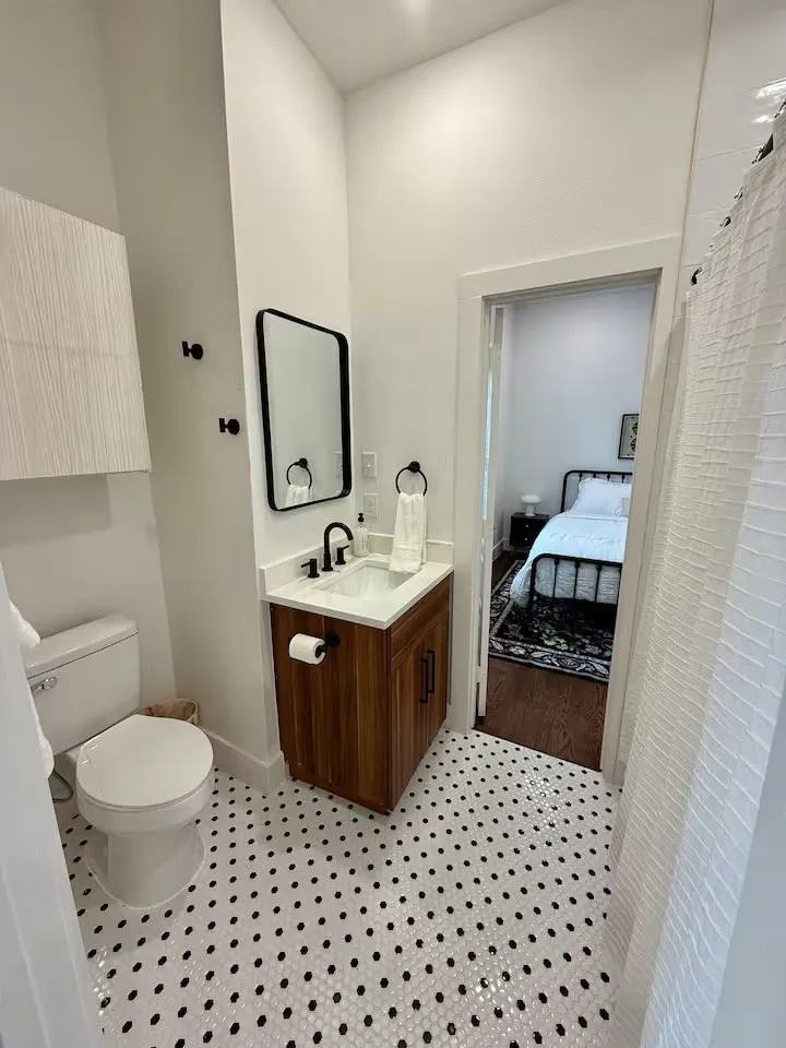 Bathroom featuring black and white penny tile flooring, a wood-finish vanity with a white countertop and rectangular sink, matte black faucet, and a wall-mounted rectangular mirror