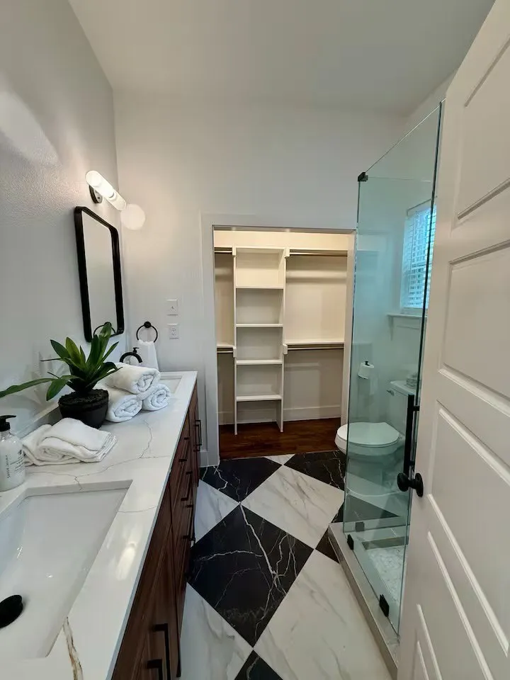 Bathroom with a black and white checkered floor, double vanity with quartz countertops, built-in shelving in the walk-in closet, and a glass-enclosed shower
