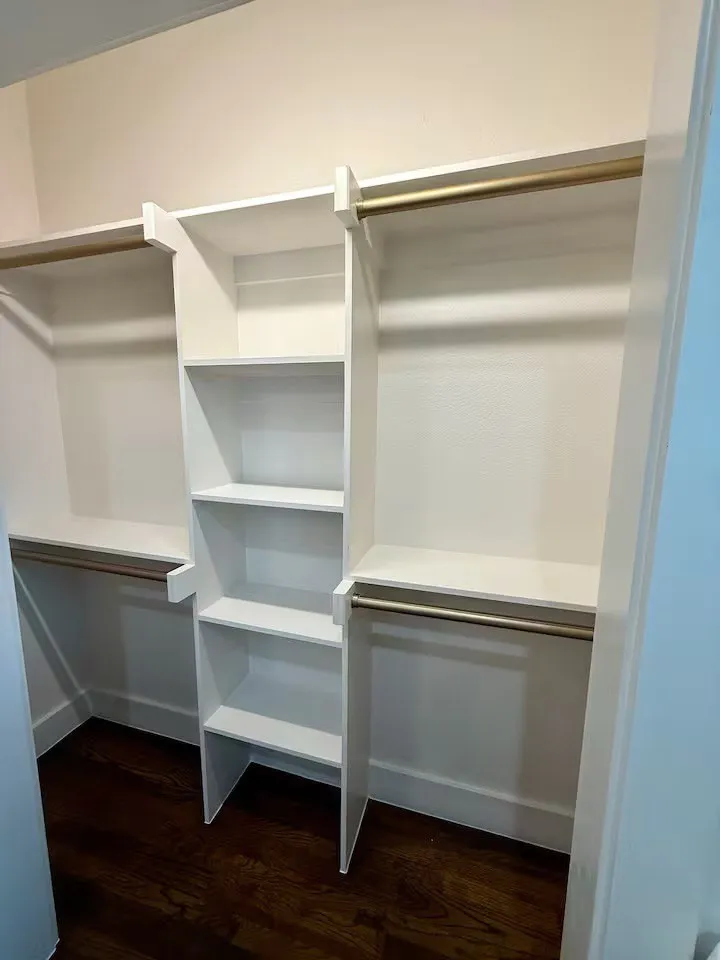 Custom closet system featuring white shelving, multiple hanging rods, and dark wood-finish flooring