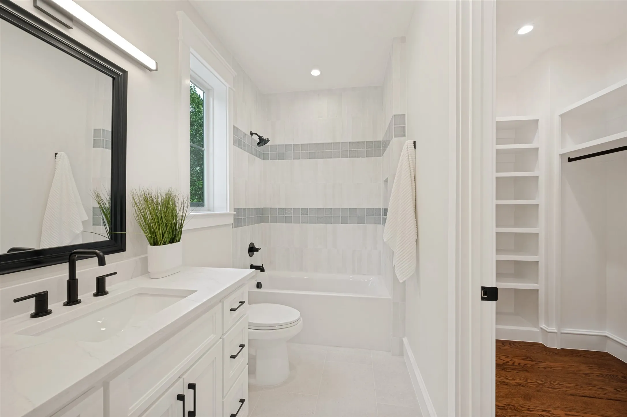 Bathroom featuring a white vanity with an integrated sink, matte black fixtures, a framed mirror, and a tub/shower combination with decorative tile banding