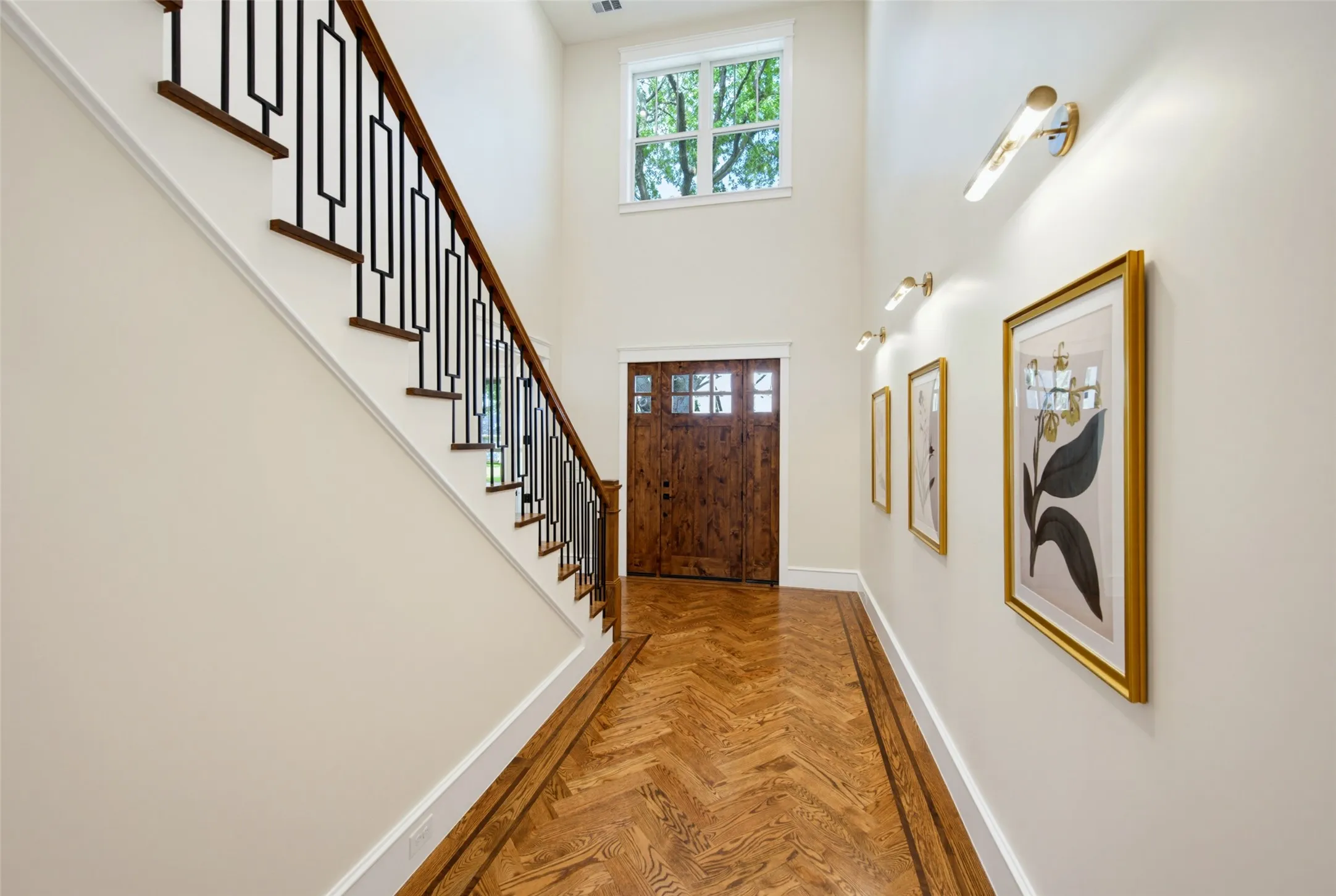 Entryway featuring high ceilings, wood-finish herringbone flooring, a decorative wood front door, and a staircase with dark wood treads and a black metal railing