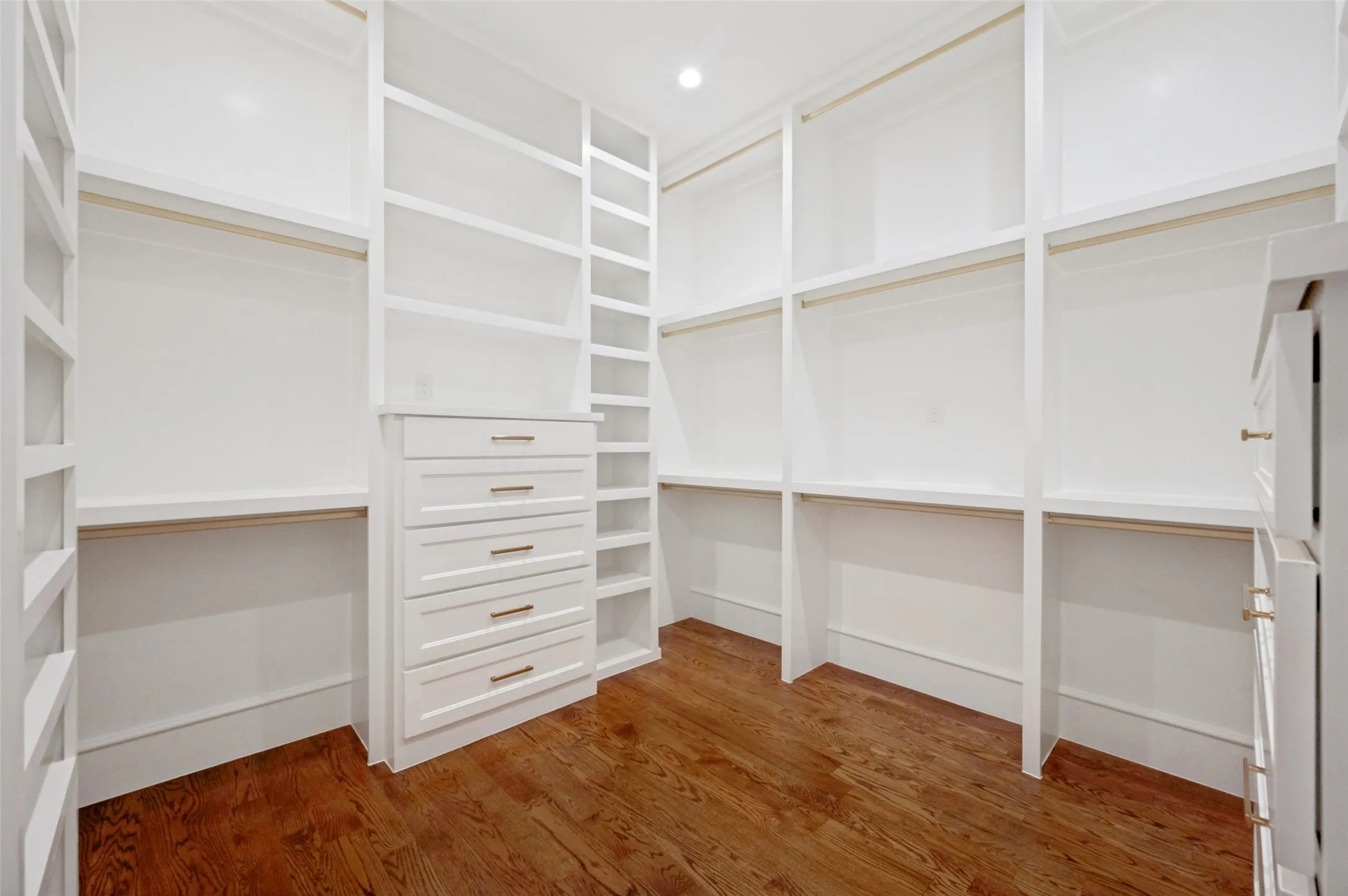 Built-in closet system featuring white cabinetry, multiple shelves, and integrated drawers with brass hardware
