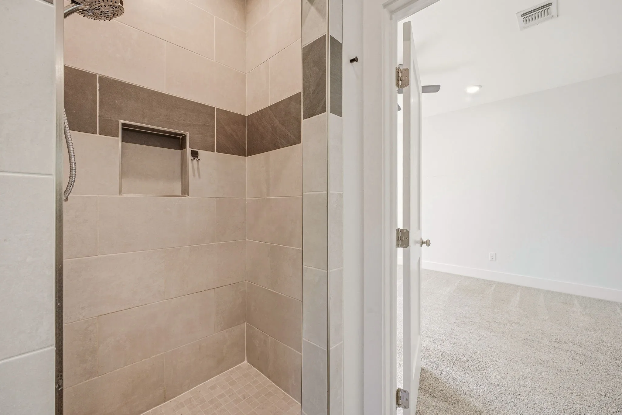 Shower enclosure with light-toned rectangular wall tiles, a contrasting dark horizontal accent band, and a built-in shower niche