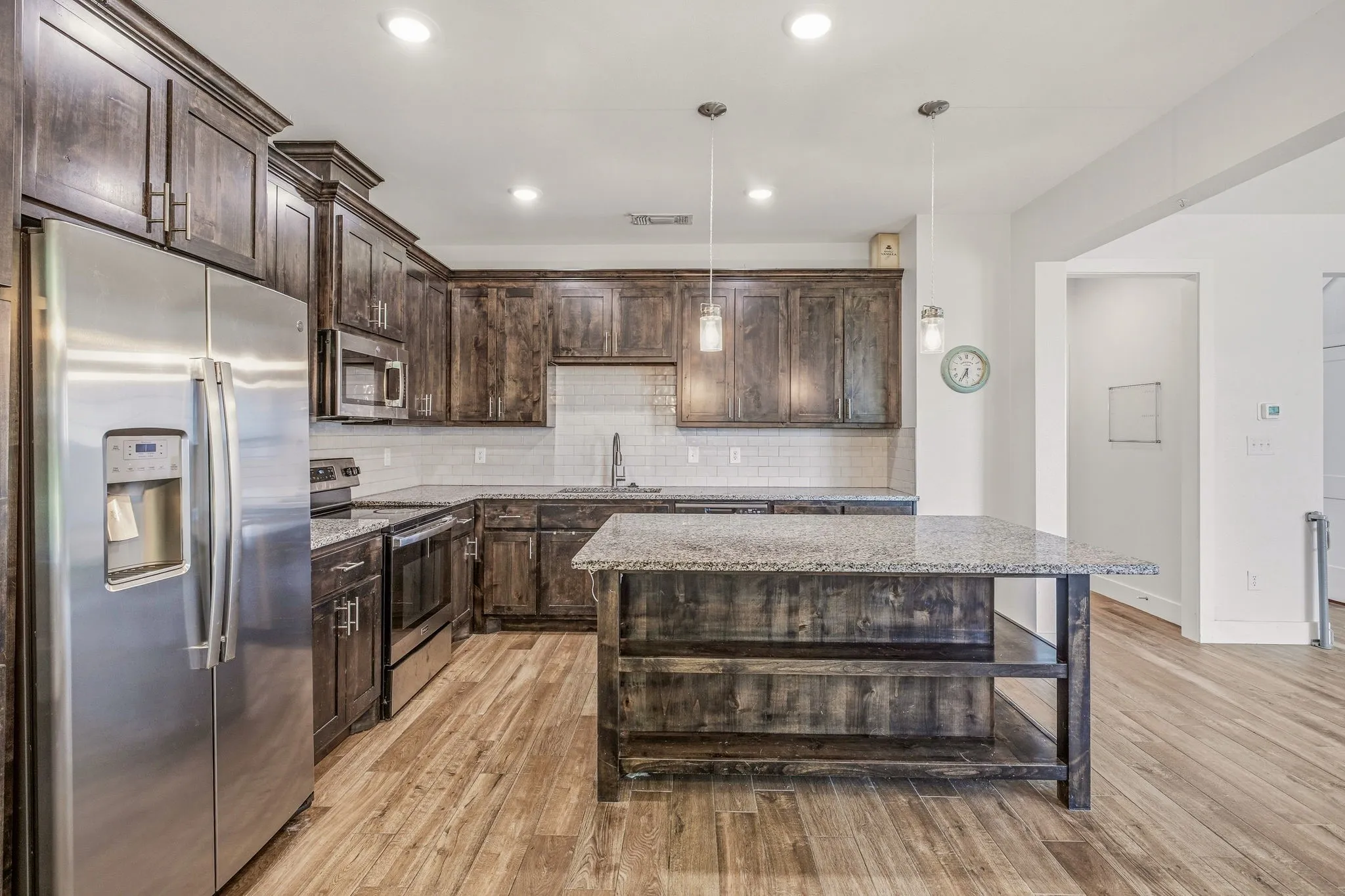 Kitchen featuring wood-finish flooring, dark wood cabinetry, stainless steel appliances, granite countertops, and a subway tile backsplash