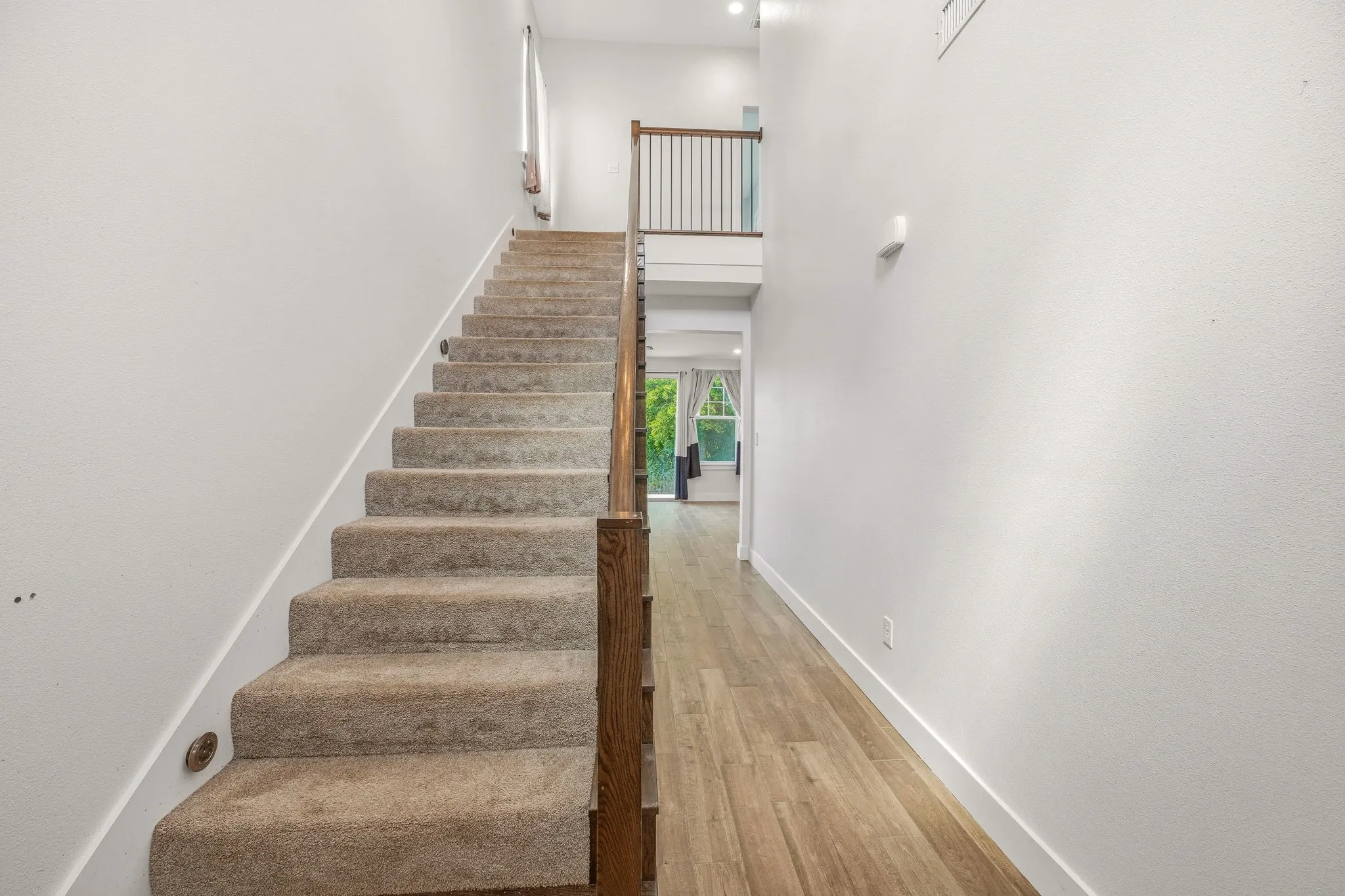 Carpeted staircase with integrated step lighting and wood handrail, featuring a second-story landing with metal balusters