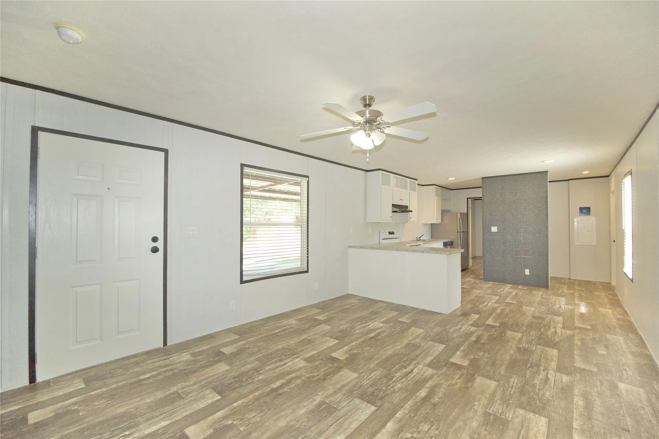 Open-concept living area featuring wood-finish flooring, a contemporary ceiling fan, and ample natural light from a prominent window