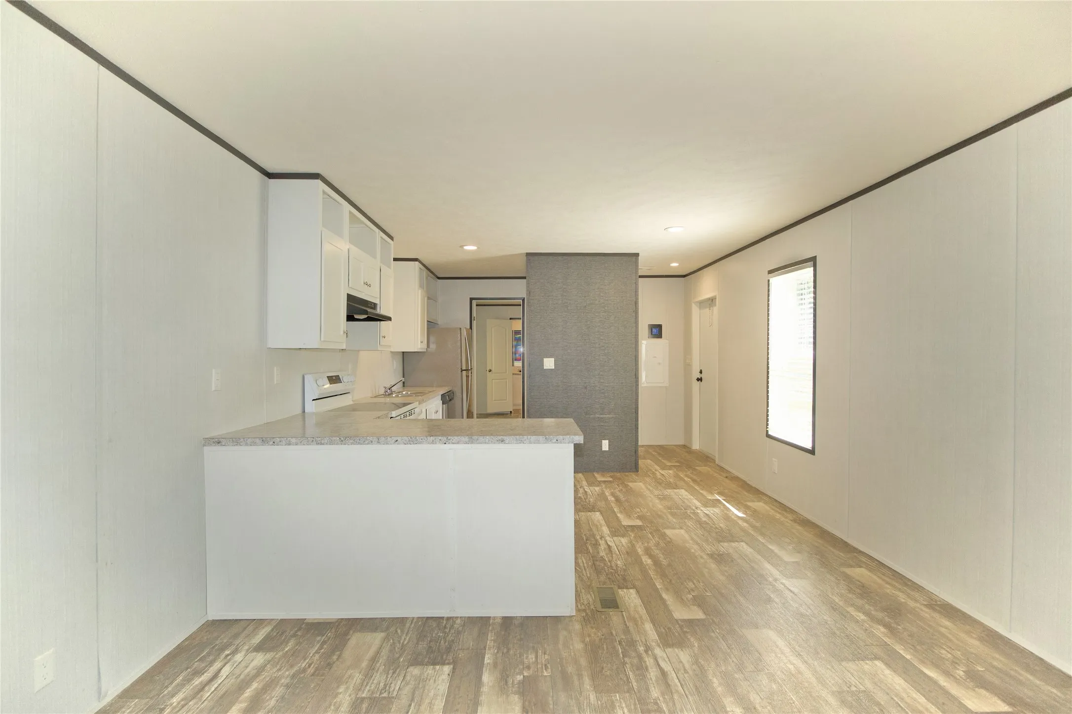 Open-concept living space with wood-finish flooring, a kitchen island with a countertop, white cabinetry, integrated range hood, and a white oven