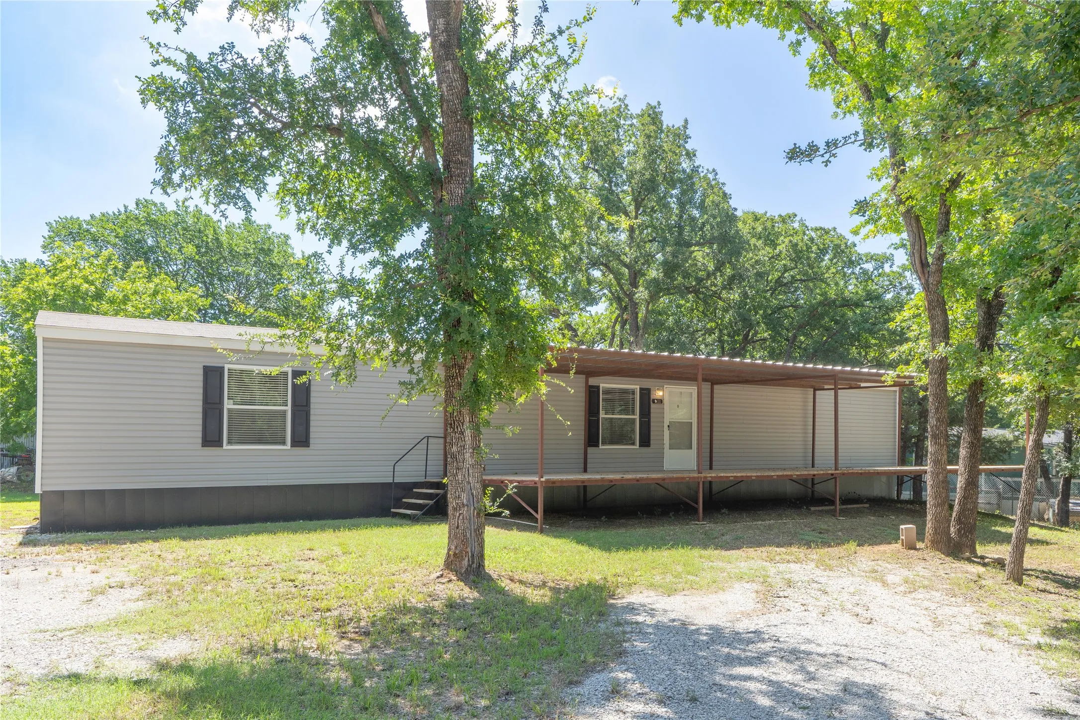 Light gray siding exterior with black shutters, featuring a covered porch extending the length of the home