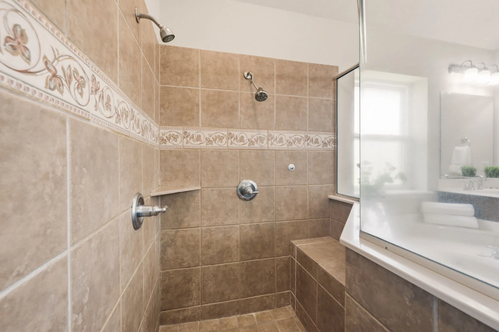 Tiled shower enclosure featuring dual showerheads, an integrated bench, and a decorative tile accent band