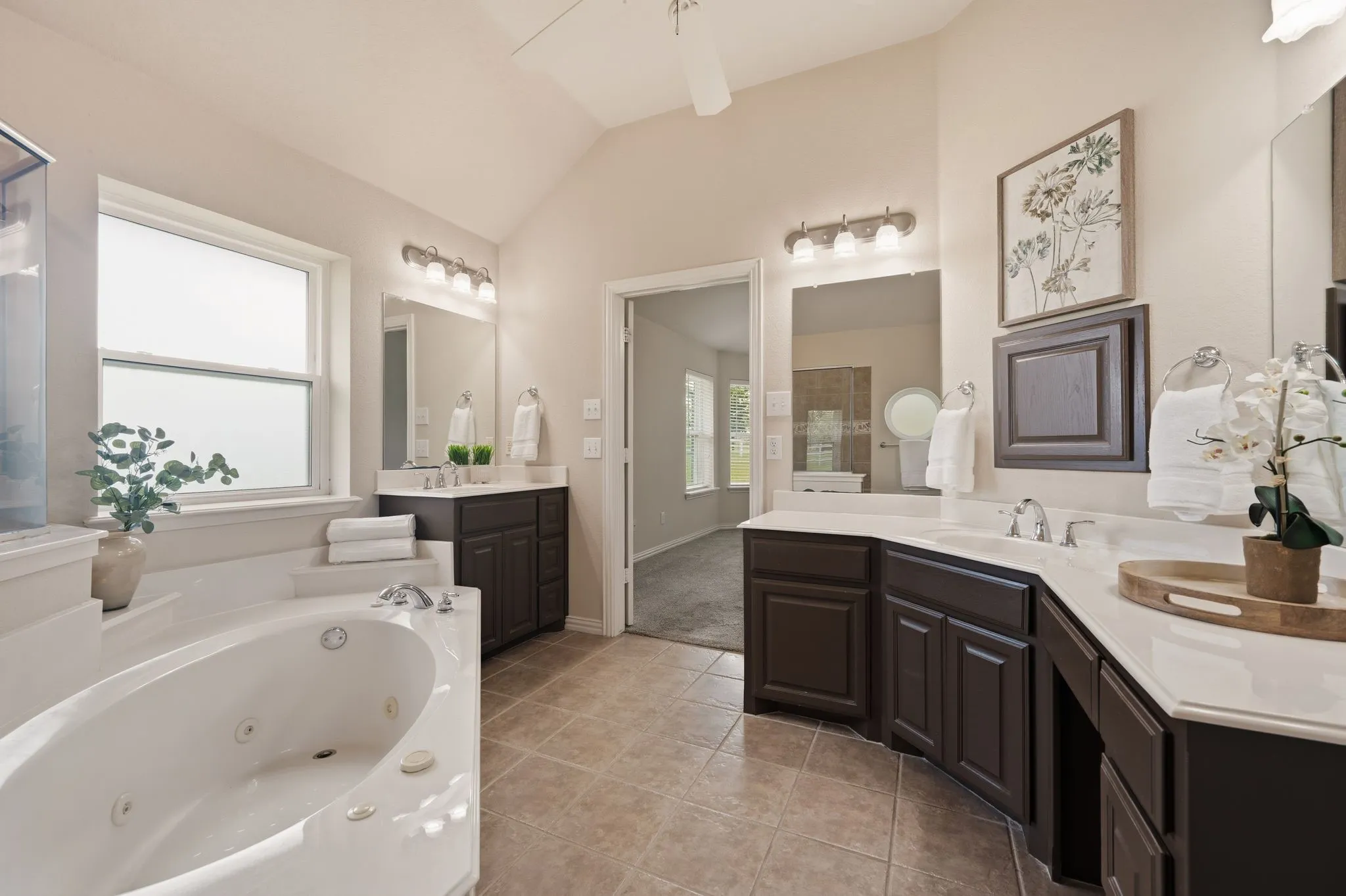 Spacious bathroom featuring a large jetted tub, dual window, dual vanities with integrated sinks, dark wood-finish cabinetry, and tiled flooring