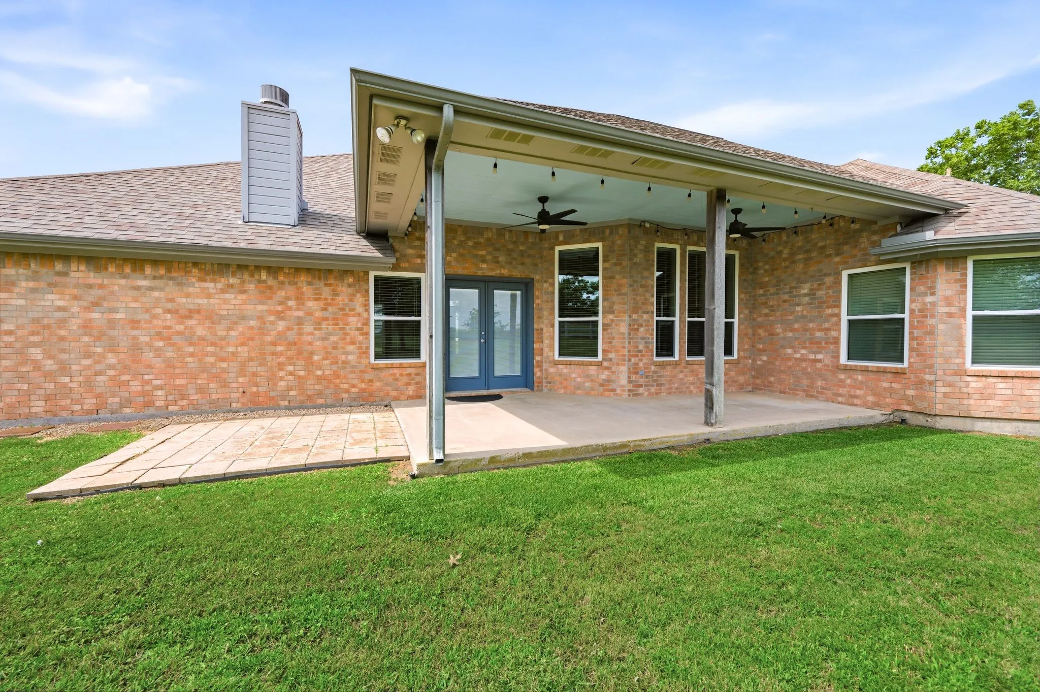 Brick exterior with a covered patio featuring a concrete floor, dual ceiling fans, and string lighting