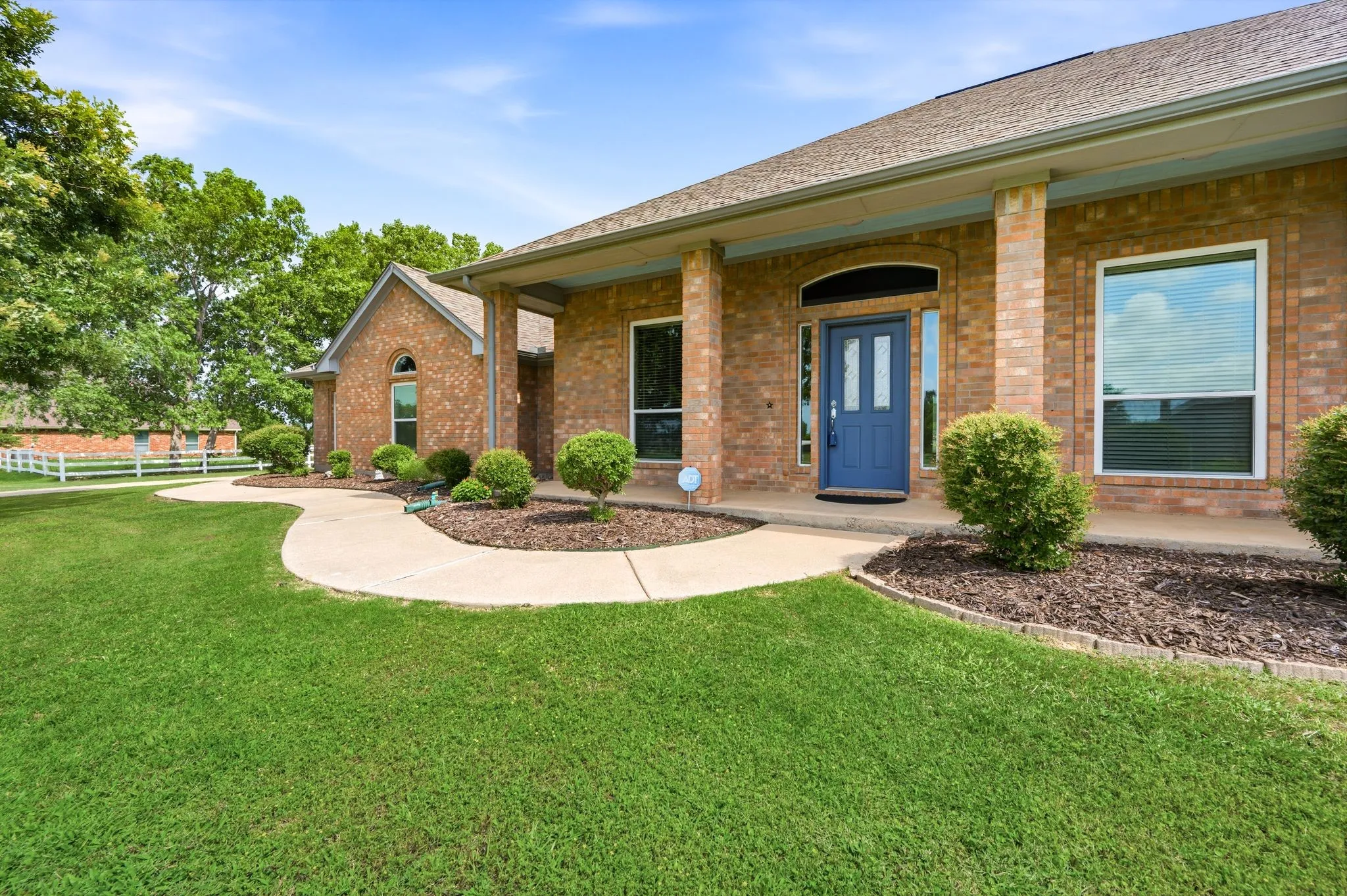 Brick exterior residence featuring a covered front porch with substantial columns, a prominent blue entry door with decorative glass inserts, and a concrete curved pathway