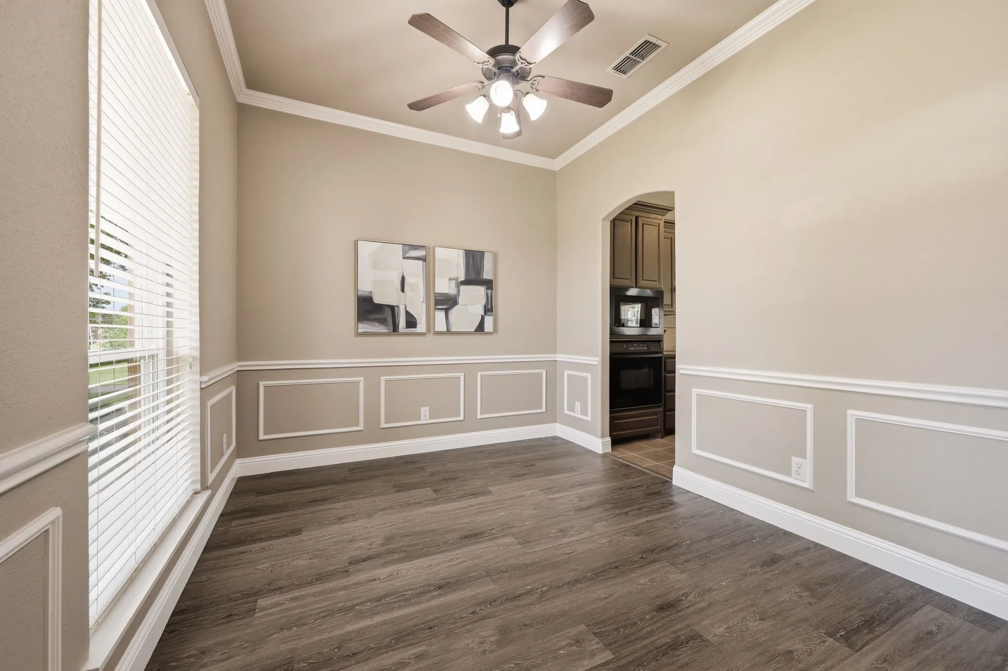 Spacious interior room featuring wood-finish flooring, wainscoting, crown molding, and a ceiling fan with integrated lighting