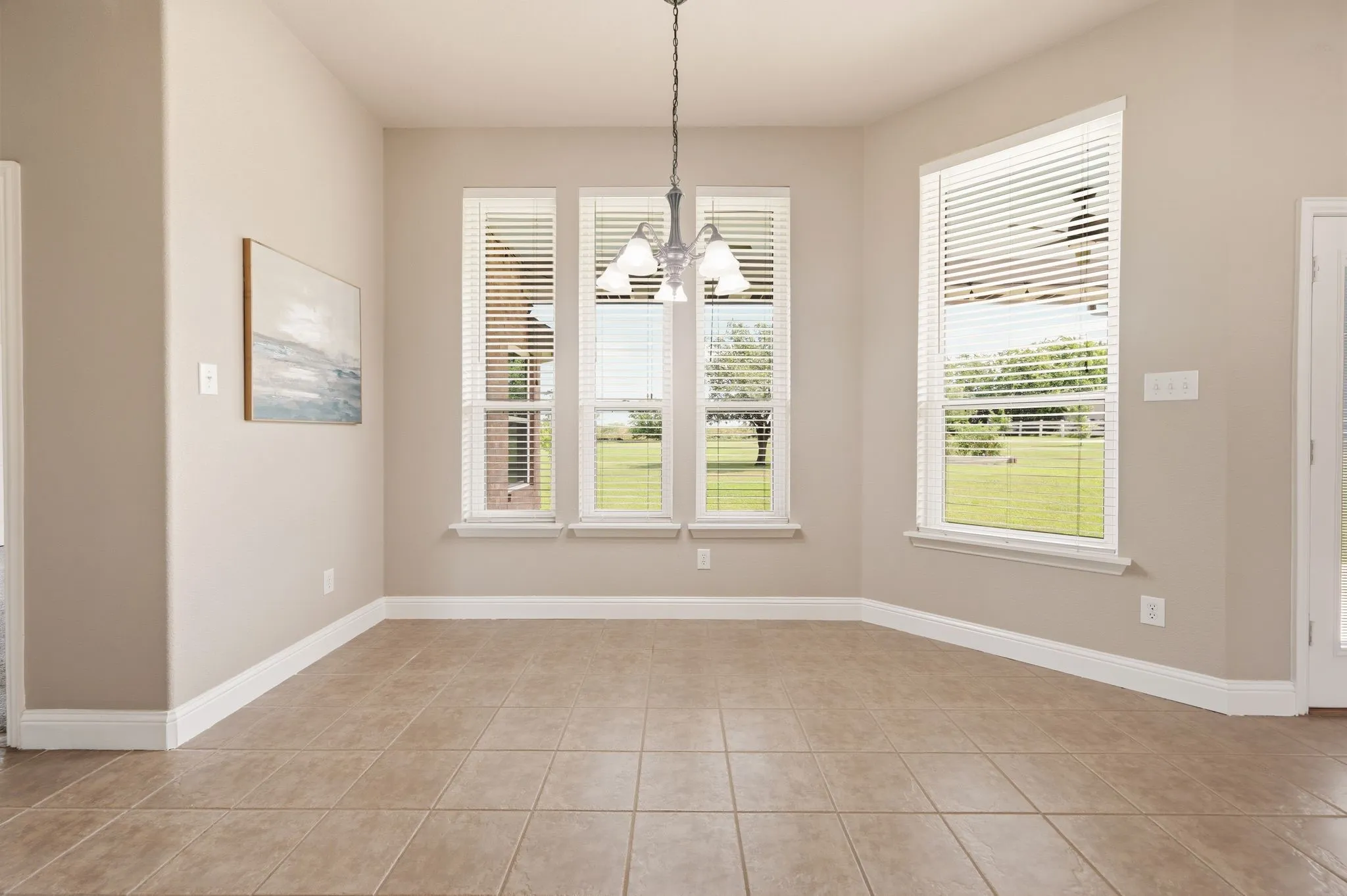 Room featuring large-format tile flooring, multiple windows with blinds, a ceiling-mounted light fixture, and neutral-toned walls with white trim