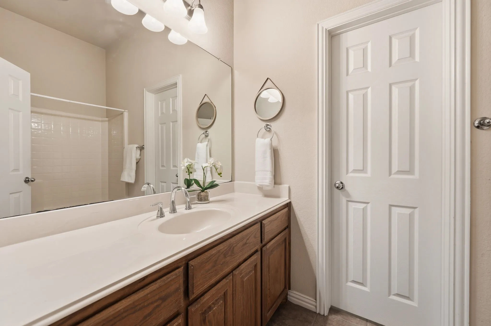 Bathroom vanity featuring an integrated sink with a chrome faucet, under-cabinet storage, and an expansive wall-mounted mirror