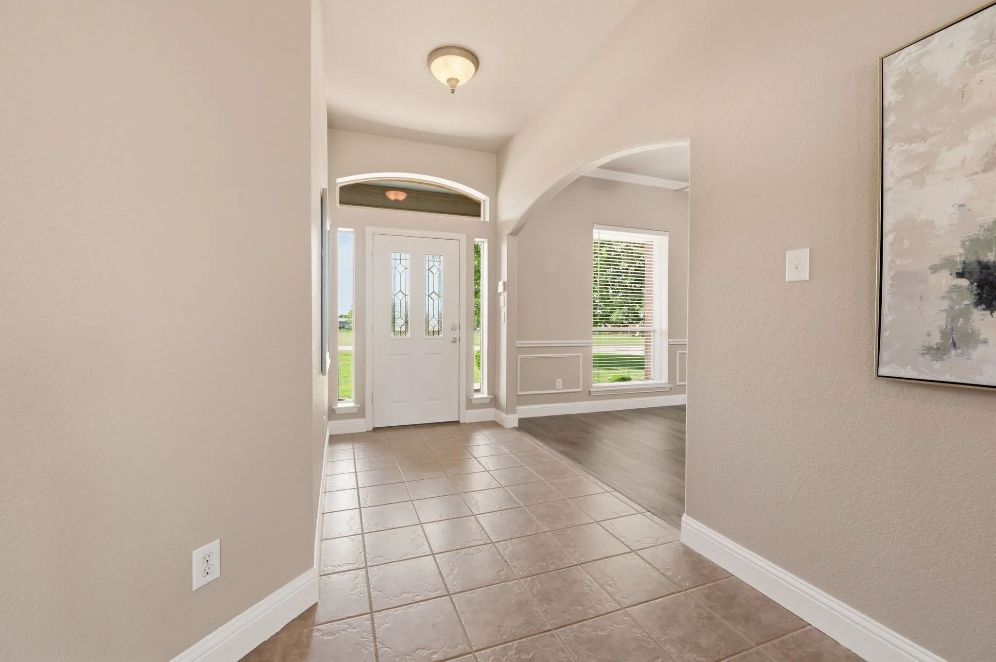 Entryway featuring tile flooring, a decorative glass front door with sidelights and transom, an arched doorway, and light wall tones