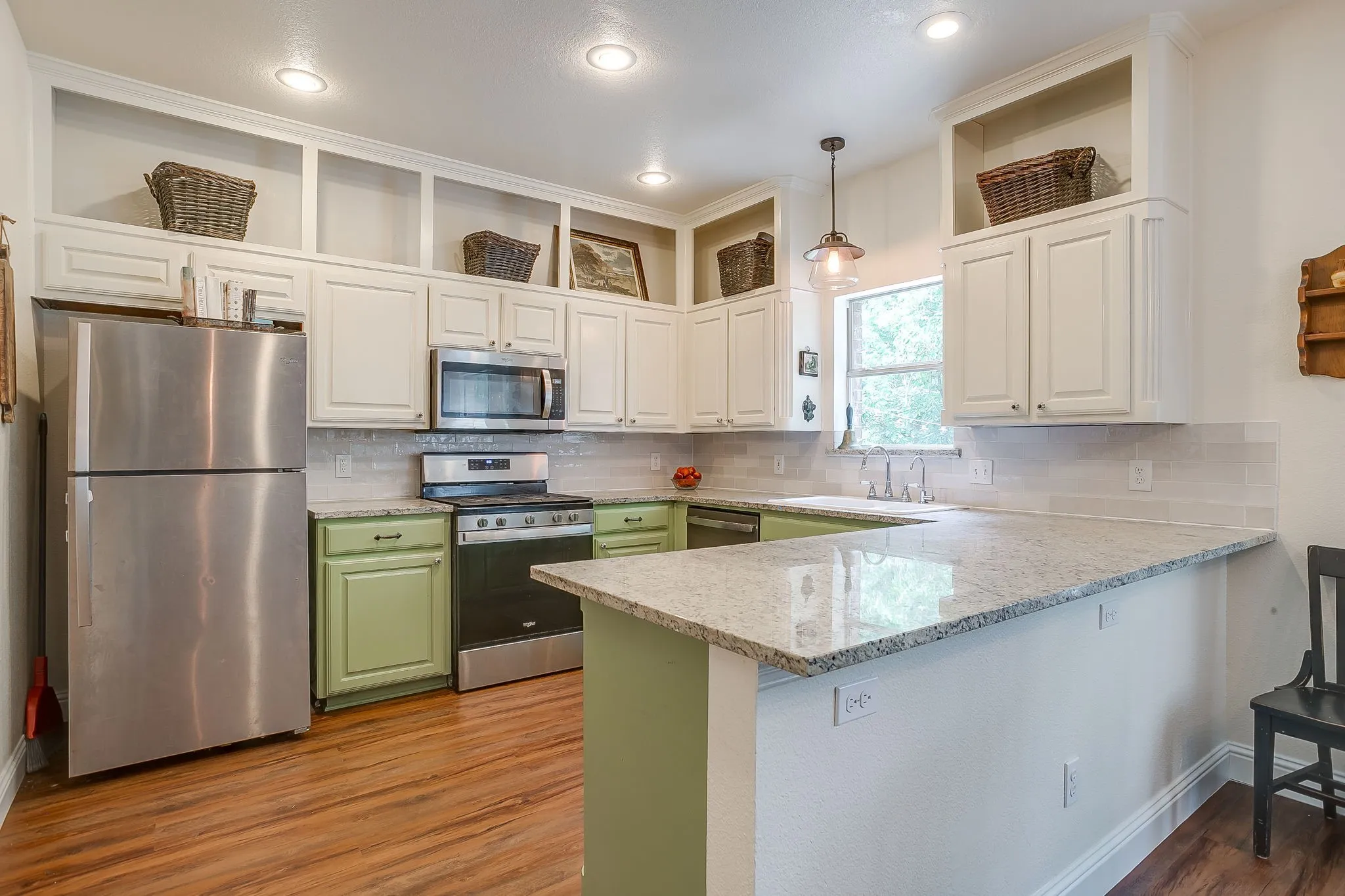 Kitchen featuring a breakfast bar with granite countertops, stainless steel appliances, light-toned cabinetry, and wood-finish flooring