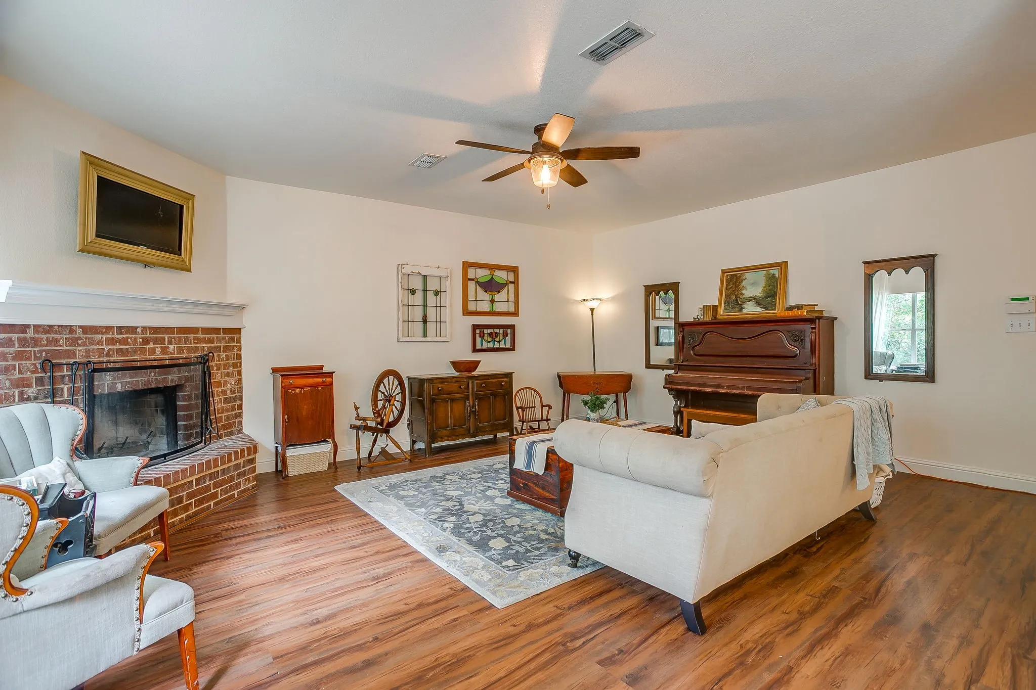 Spacious living area featuring a brick fireplace with a white mantle, wood-finish flooring, and a ceiling fan