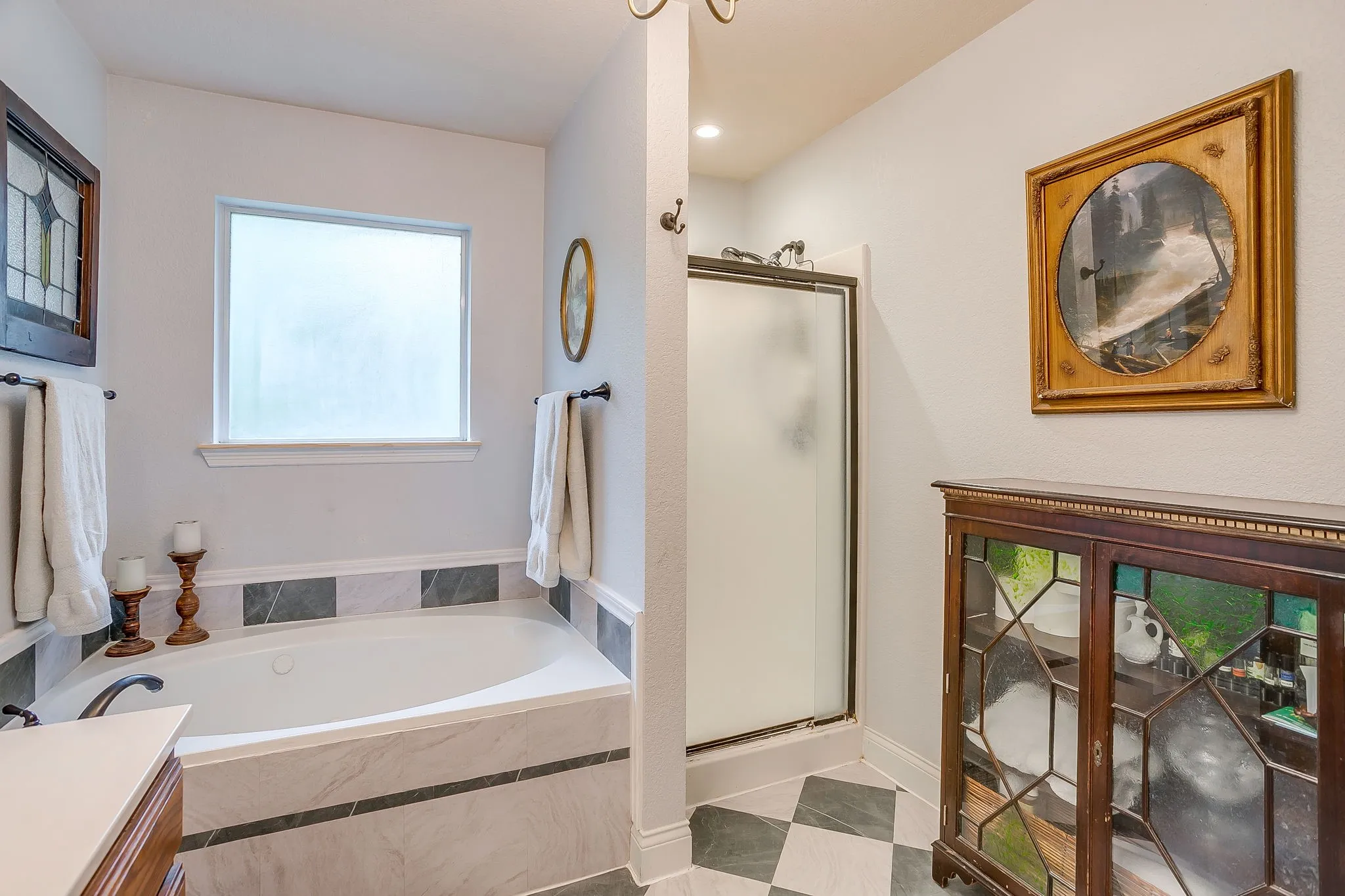 Soaking tub with a tiled surround, frosted window, and a separate shower enclosure