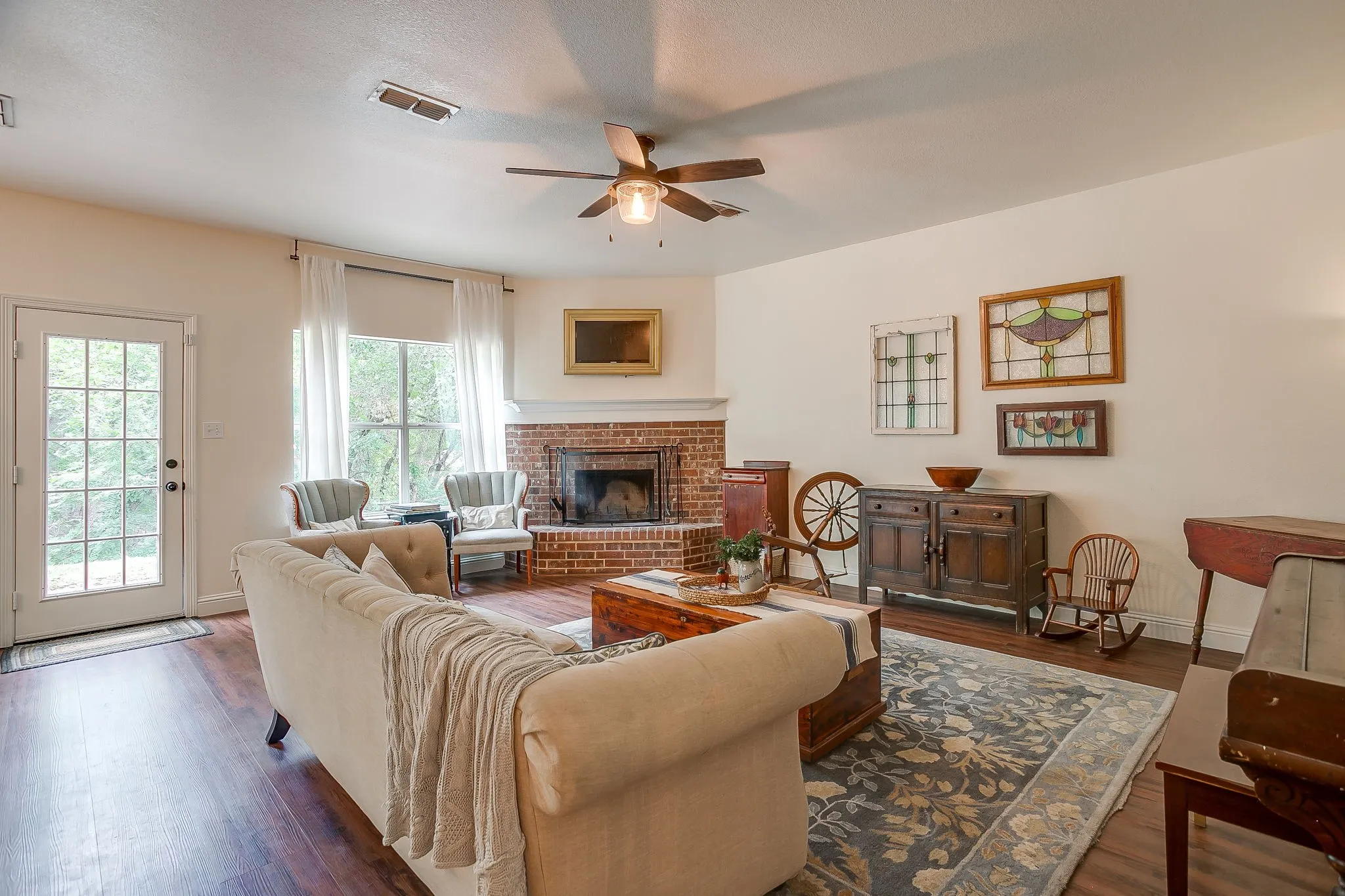 Living area featuring dark wood-finish flooring, a ceiling fan, and a corner brick fireplace