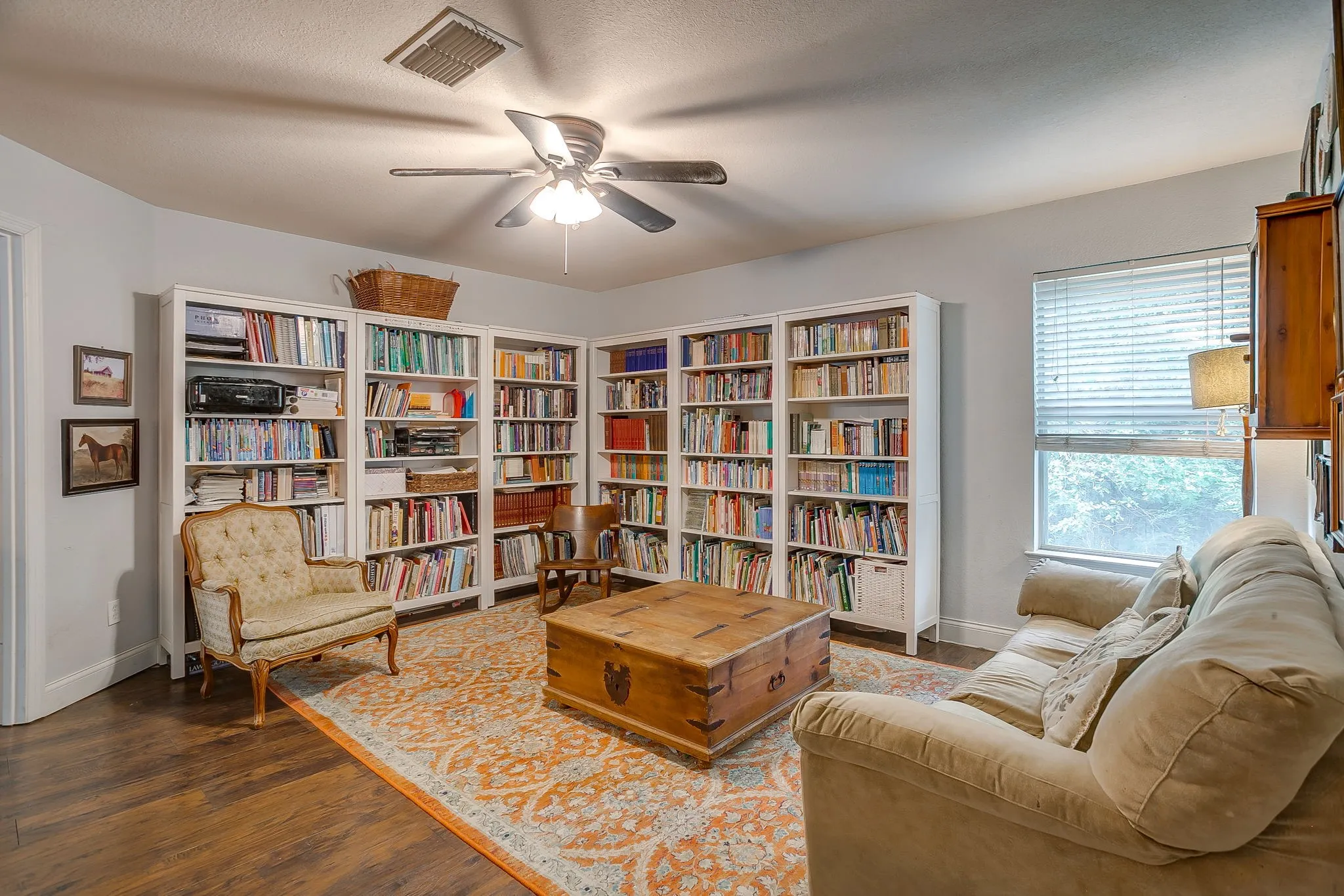 Spacious room featuring extensive built-in shelving, wood-finish flooring, a ceiling fan, and window with blinds