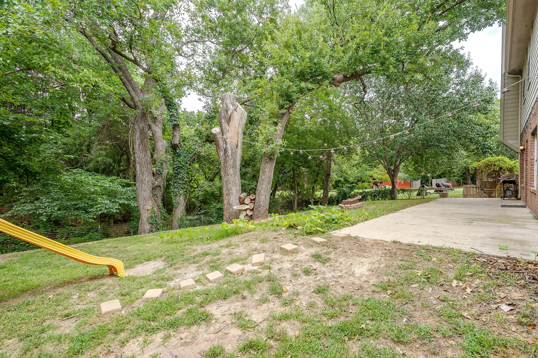 Expansive backyard featuring a concrete patio, a terraced lawn, and mature trees