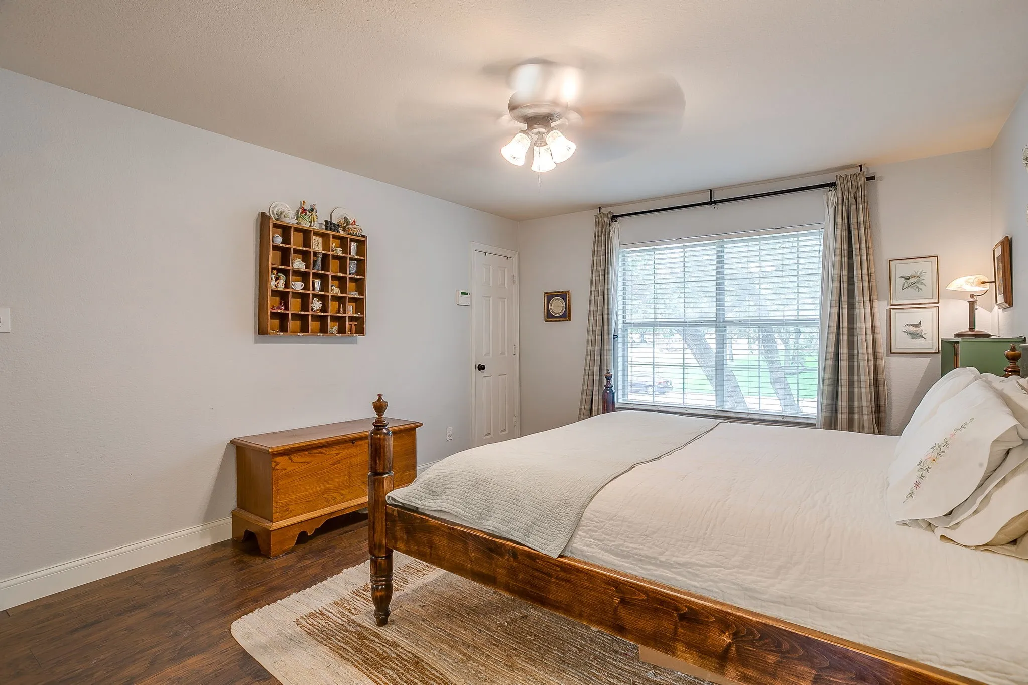Spacious room featuring wood-finish flooring, a large window with blinds, and a ceiling fan with integrated lighting