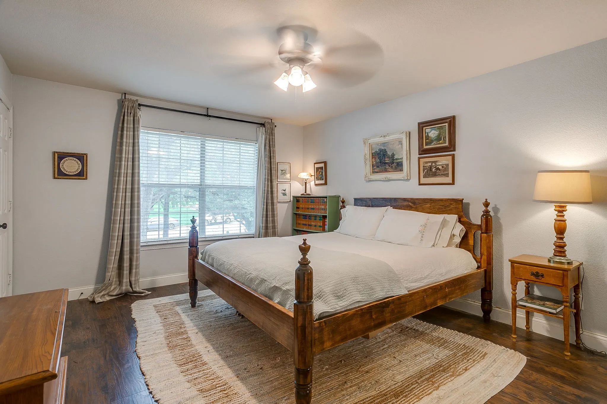 Spacious room featuring dark wood-finish flooring, a large window with blinds, a ceiling fan with integrated lighting, and neutral wall tones