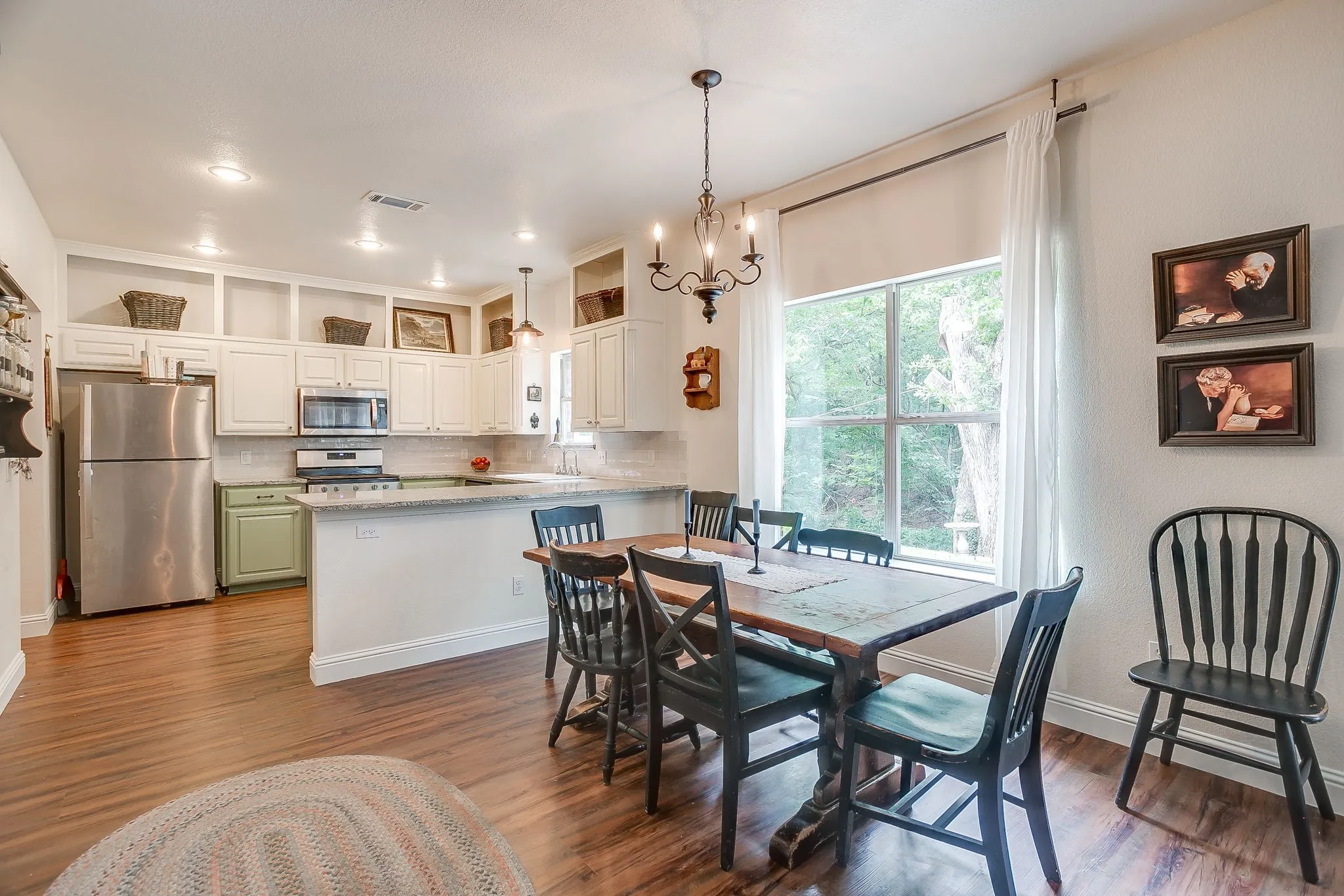 Kitchen and dining area featuring wood-finish flooring, white cabinetry with open shelving, stainless steel appliances, a tile backsplash, and a window with white curtains