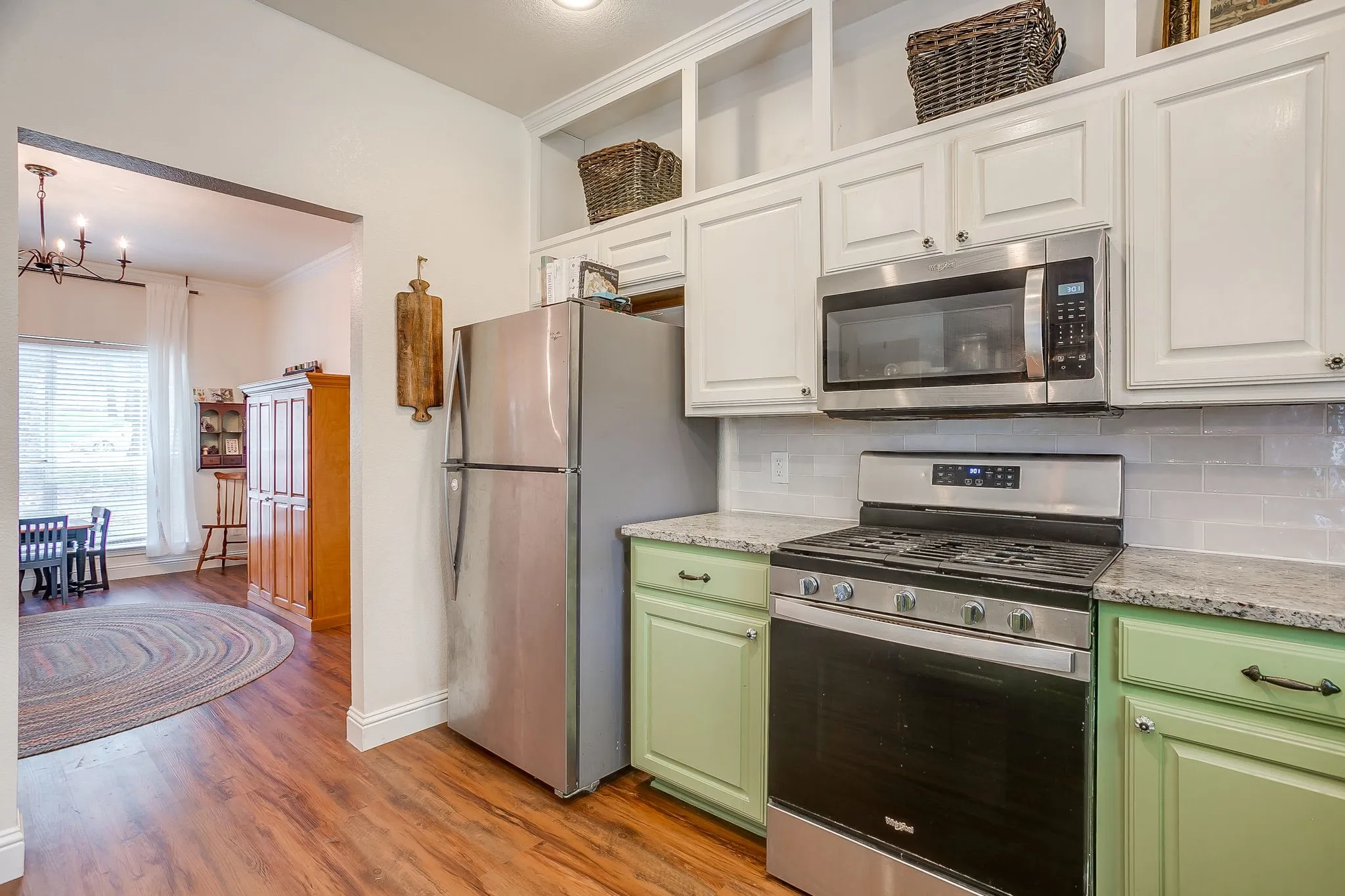 Kitchen featuring wood-finish flooring, stainless steel appliances, white subway tile backsplash, and two-tone cabinetry with light green base cabinets and white upper cabinets