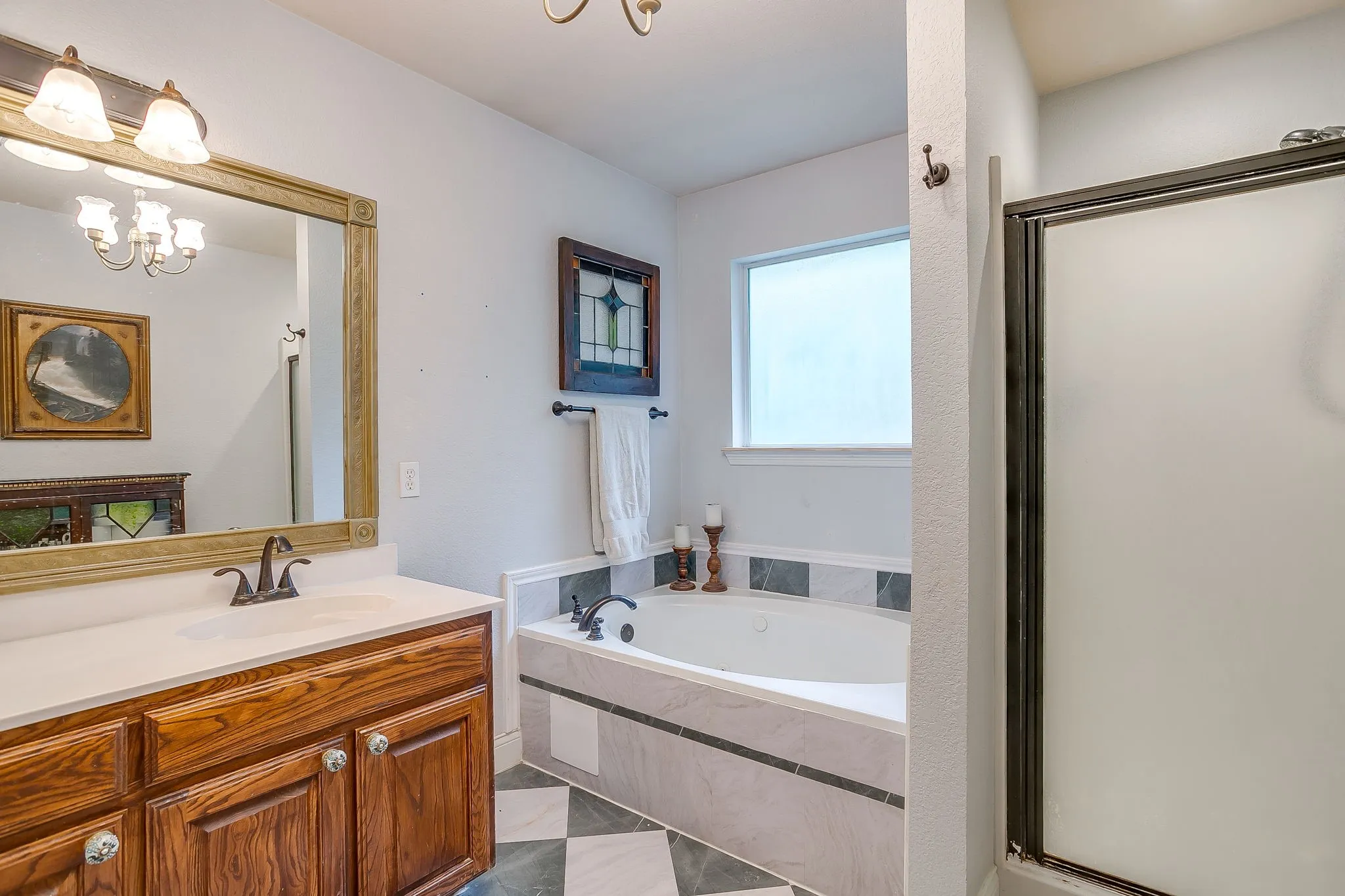 Bathroom featuring a built-in jetted tub, a separate shower enclosure with a frosted glass door, a wood-finish vanity with a light-colored countertop, and a checkerboard floor tile pattern
