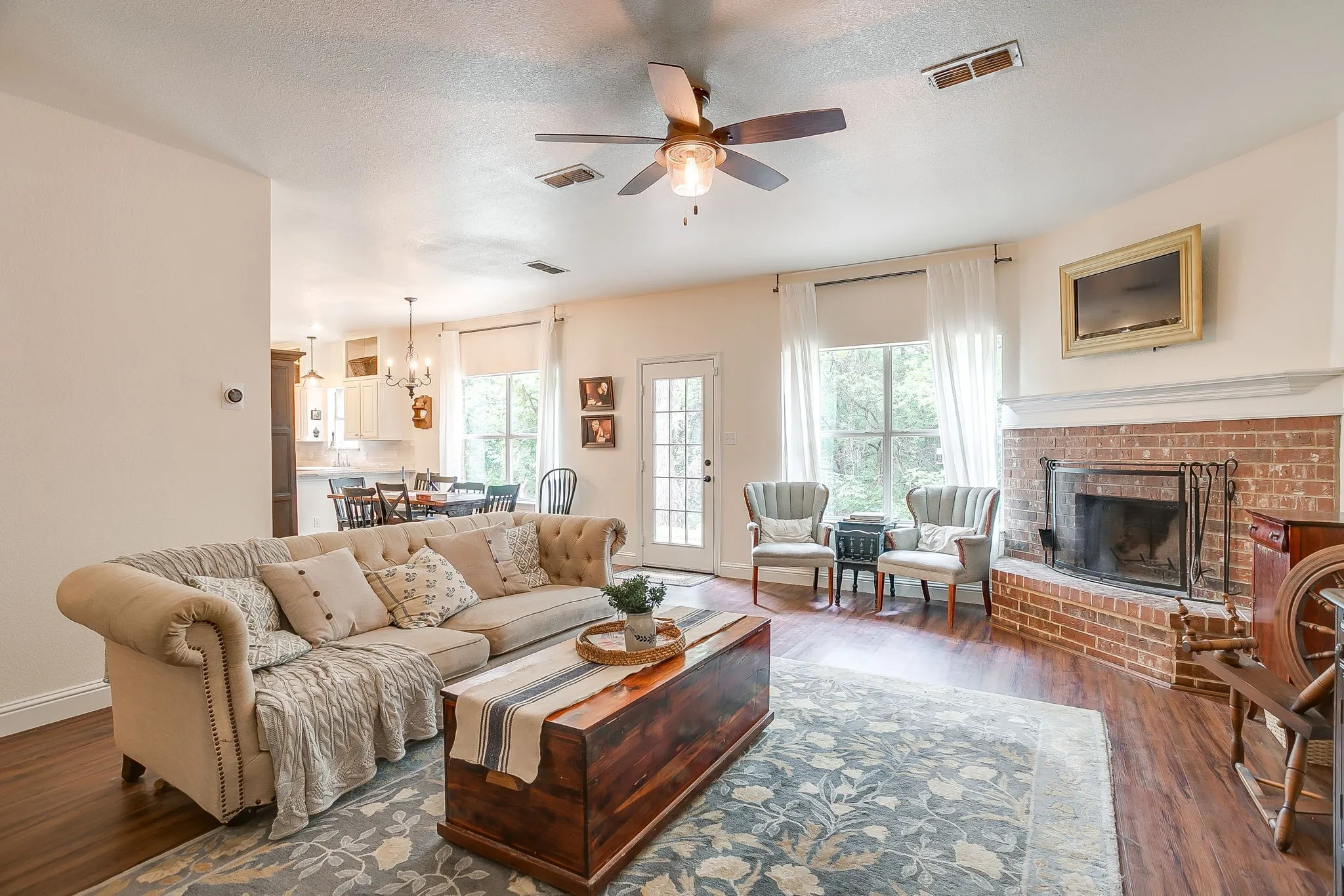 Spacious living area featuring wood-finish flooring, a ceiling fan, and a brick fireplace