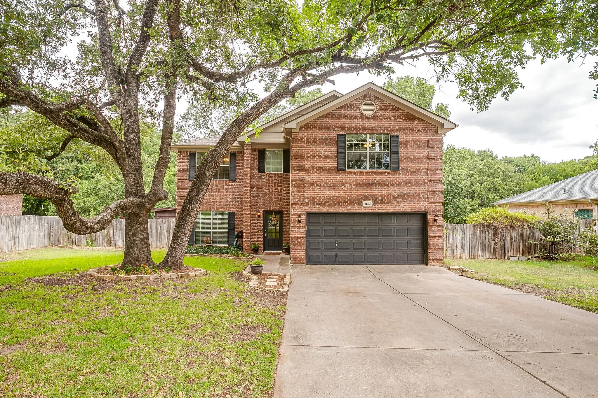 Traditional brick exterior featuring a two-story design, an attached garage with a dark panel door, and multiple windows with dark louvered shutters