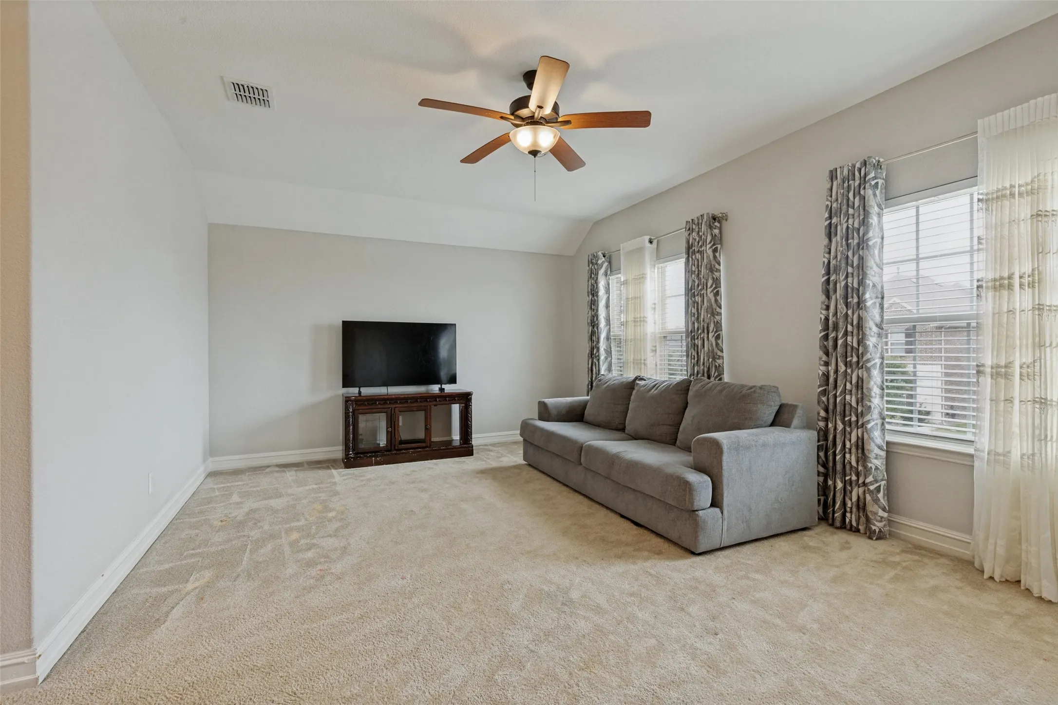 Carpeted interior space featuring a ceiling fan with integrated lighting, multiple windows with blinds, and neutral wall tones