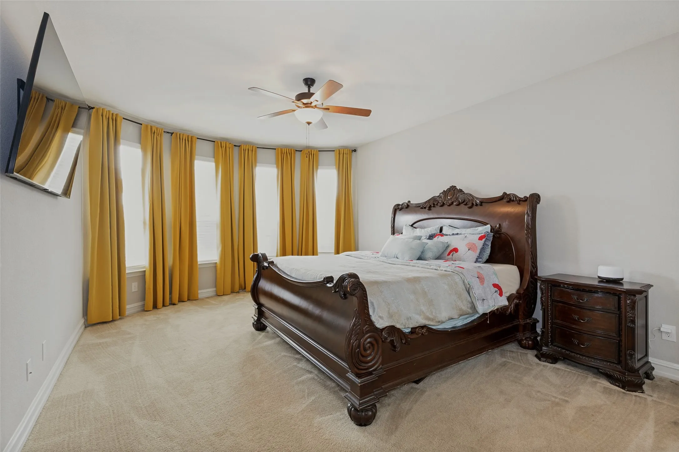 Spacious room featuring a curved bay window with multiple vertical windows, light-toned carpet flooring, and a ceiling fan with integrated lighting