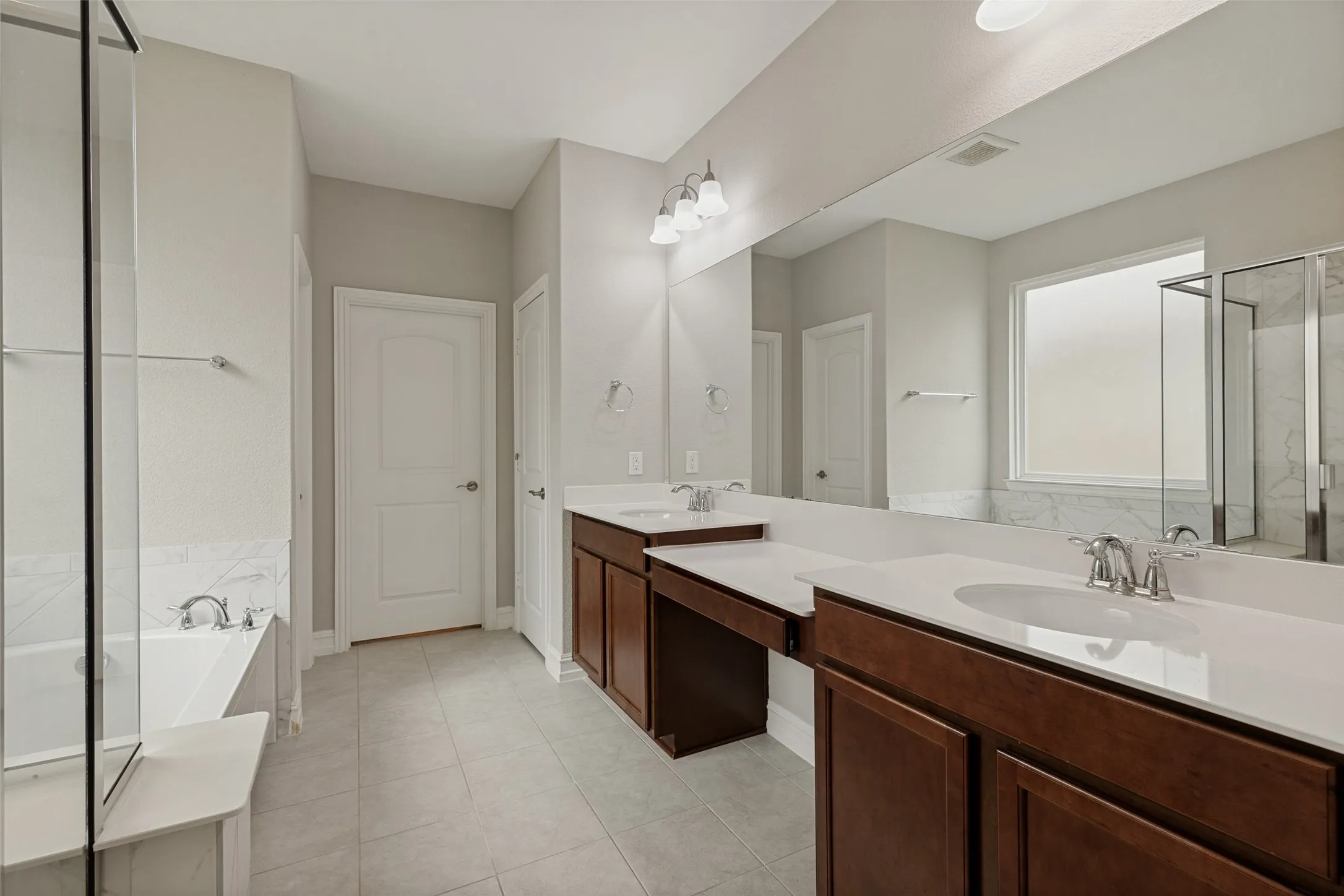 Dual vanity with dark wood cabinetry and white countertops, featuring a large mirror and overhead lighting