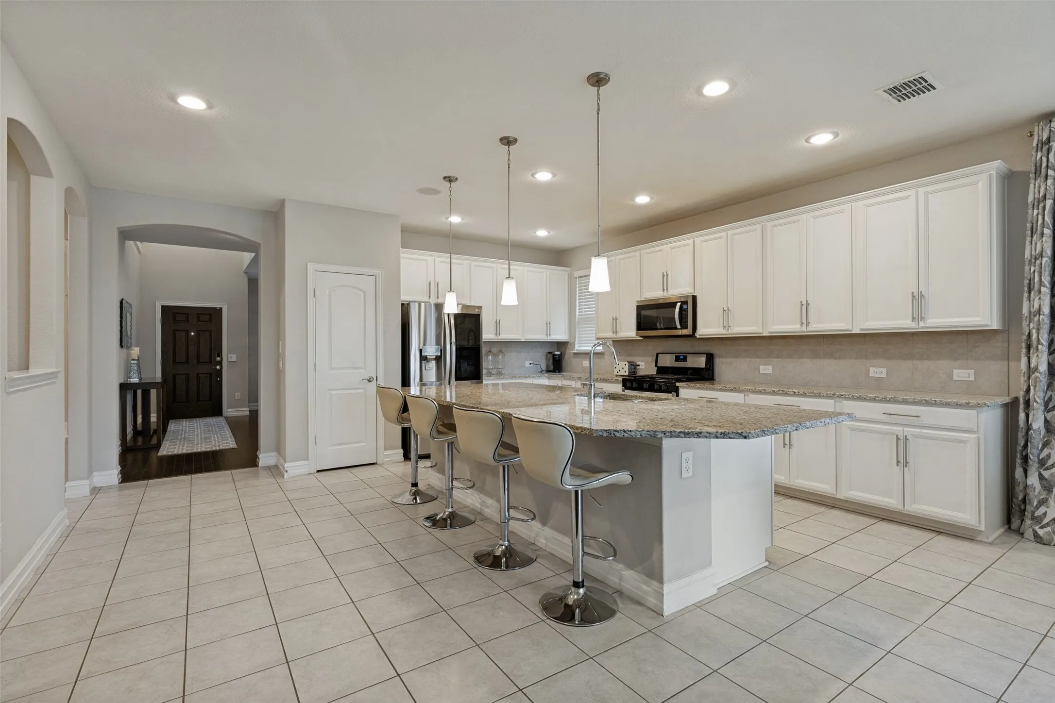 Spacious kitchen featuring a large island with seating, white cabinetry, granite countertops, and stainless steel appliances